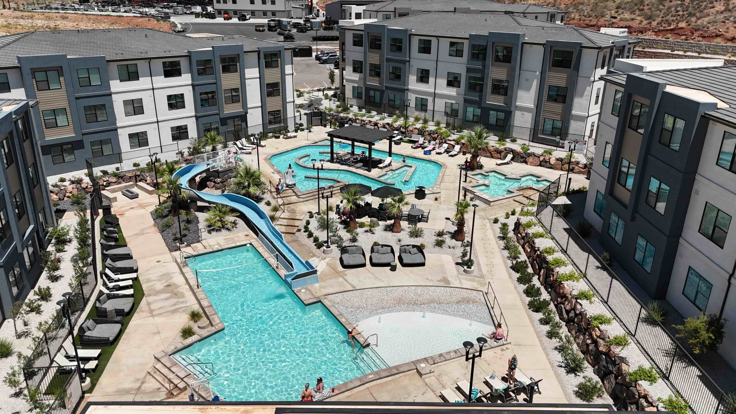 Aerial view of Terra’s pool area, with a waterslide, spa, shaded seating and lounge chairs surrounded by condo buildings.