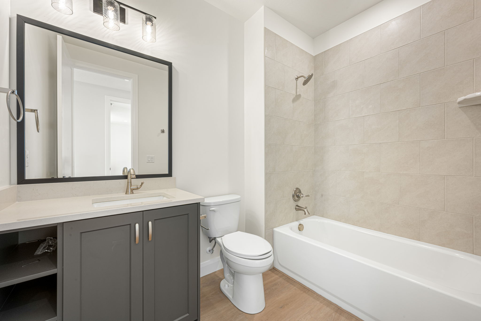 Modern bathroom featuring a dark gray vanity, white countertop, black-framed mirror, and tiled bathtub and shower combination