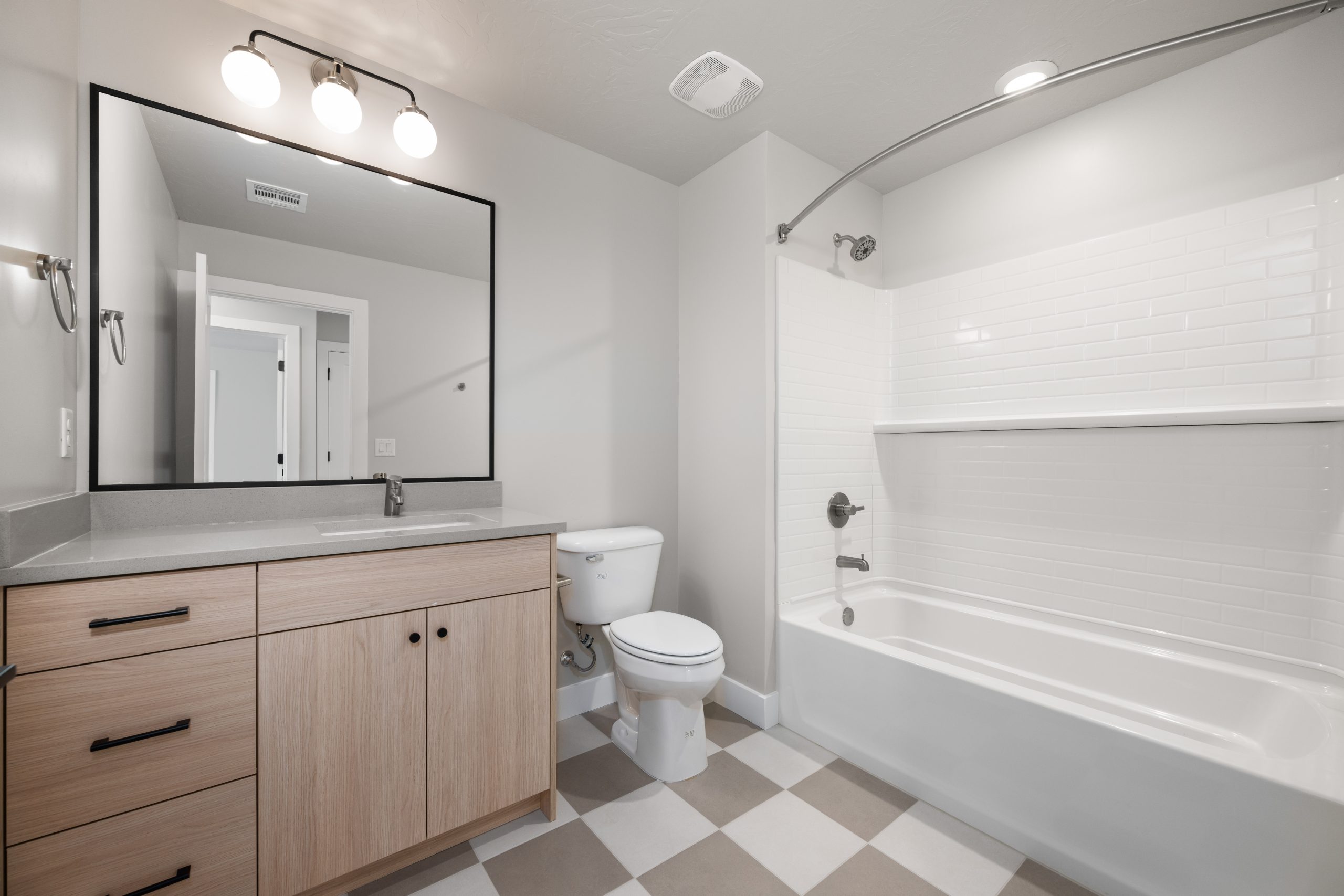 Modern bathroom featuring a light wood vanity, white subway tile bathtub shower, and checkered tile flooring in the Sunrise floor plan by Cole West.