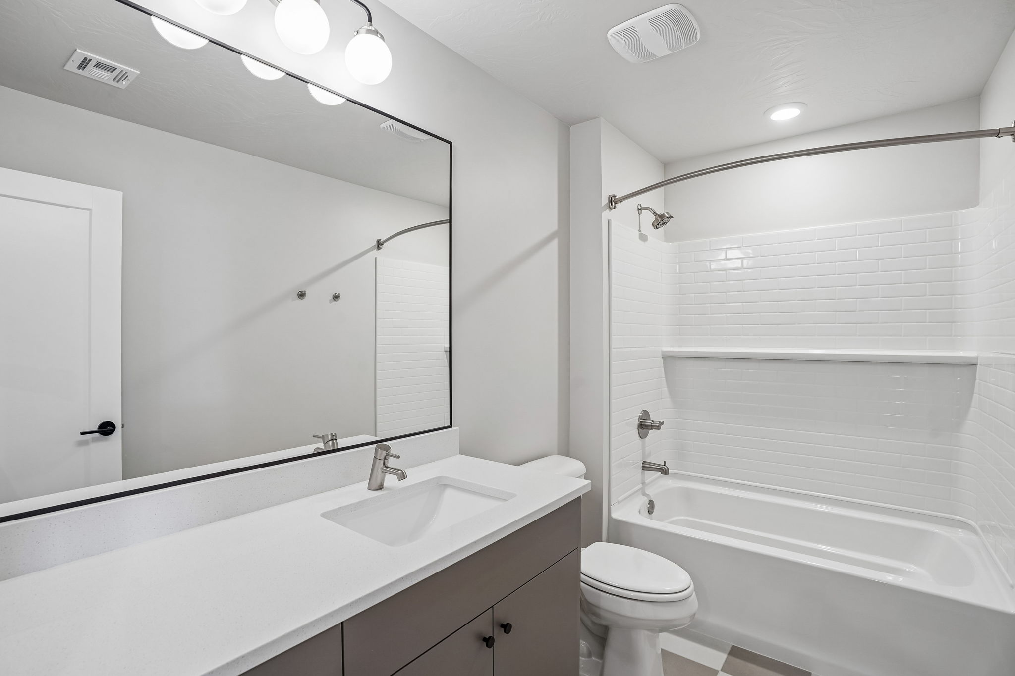 Modern bathroom in the Sunburst floor plan at Rise by Cole West in Washington, Utah, featuring a white vanity, large mirror, and tiled bathtub shower.