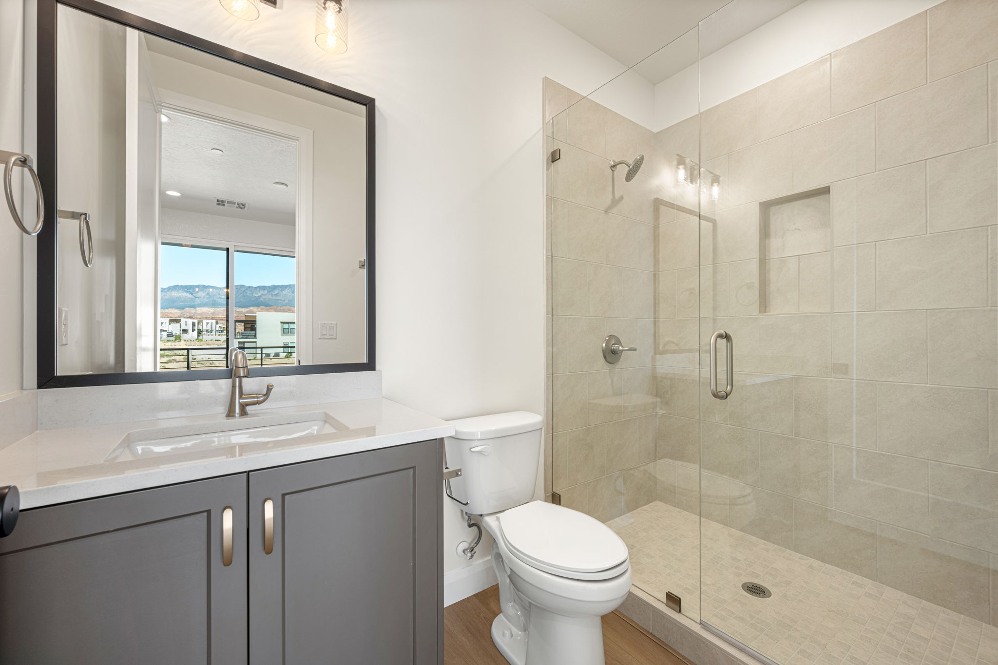 Contemporary bathroom with a gray vanity, white countertop, and glass-enclosed walk-in shower with neutral tile finishes.