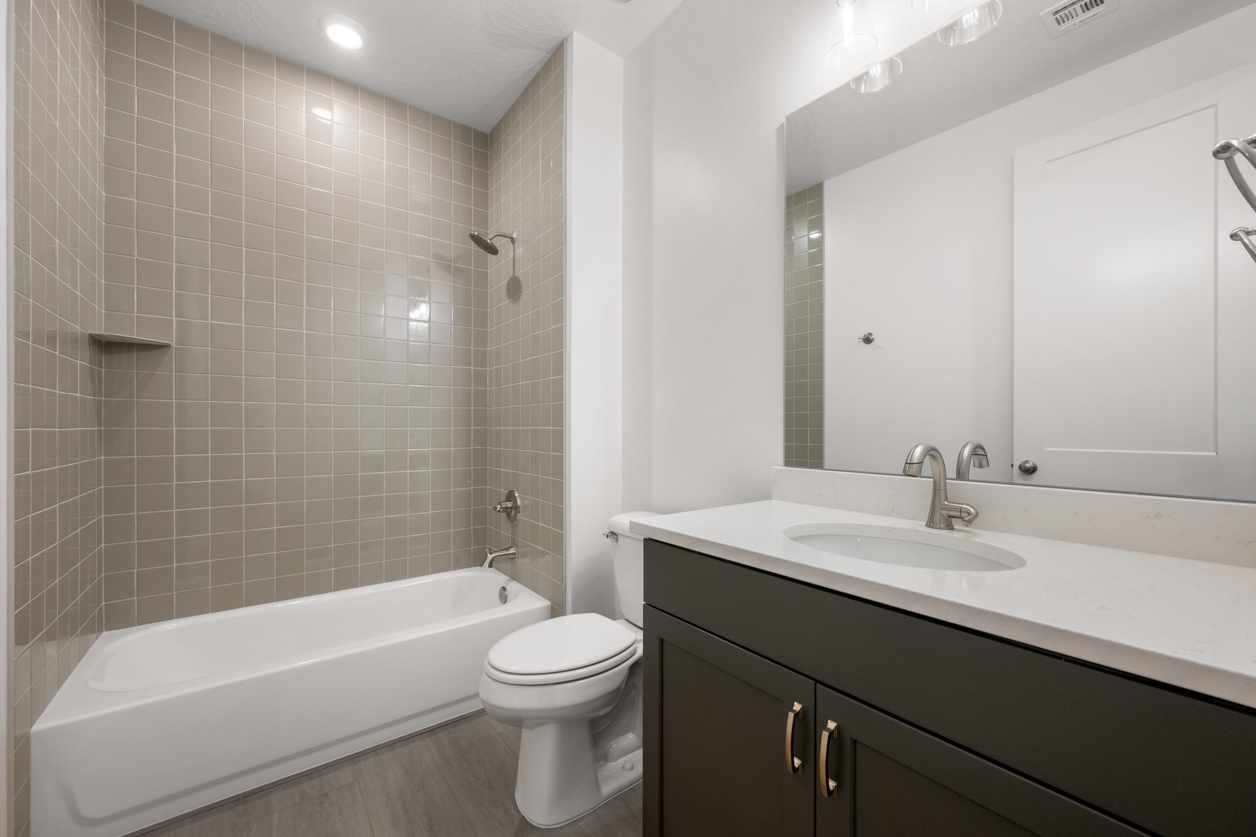 Modern guest bathroom in the Mesa home at Solis by Cole West, featuring a tiled bathtub surround, dark vanity cabinetry, and white countertops.