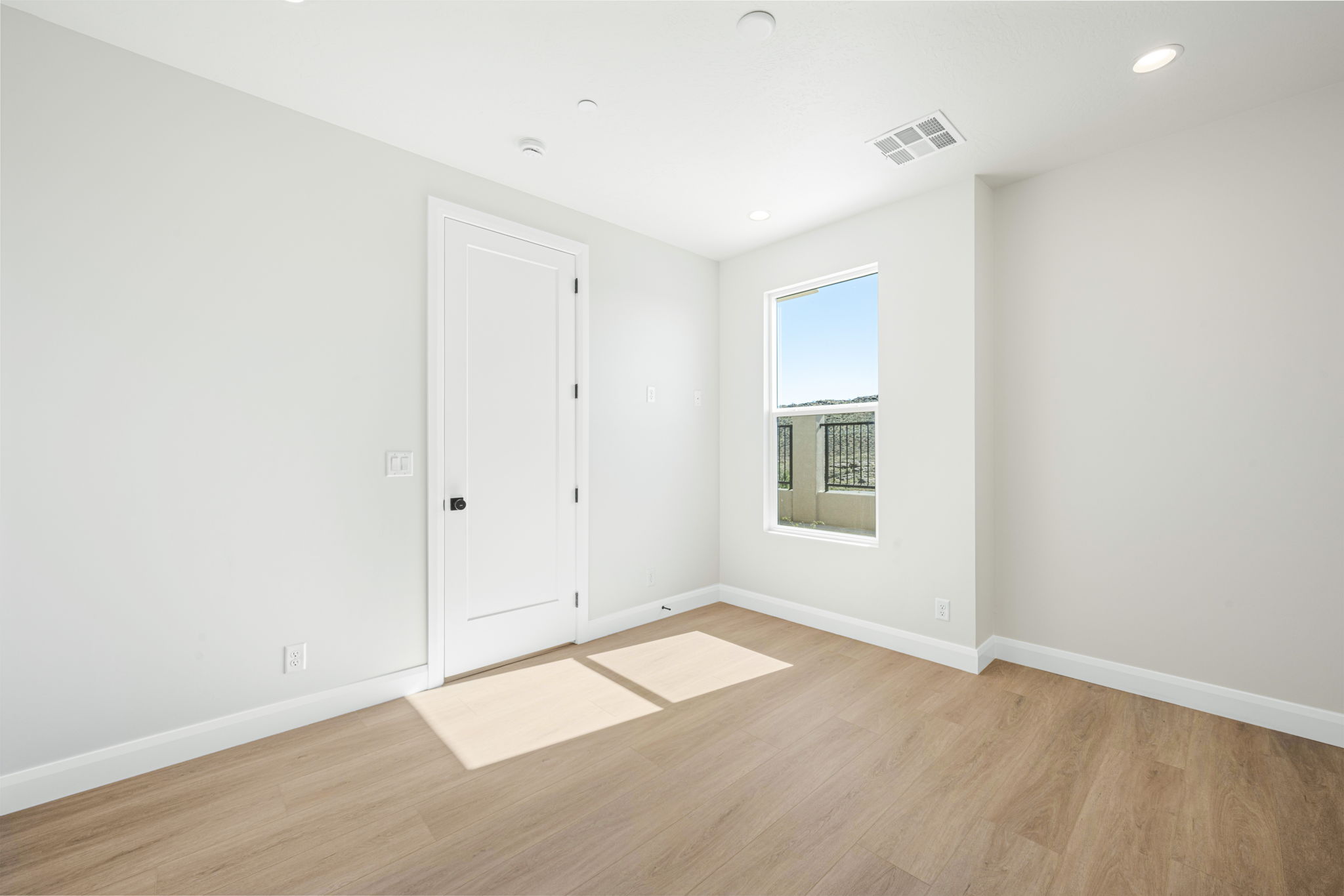 Bright bedroom in the Bahama floor plan featuring wood-look flooring, white walls, and a large window overlooking the community.