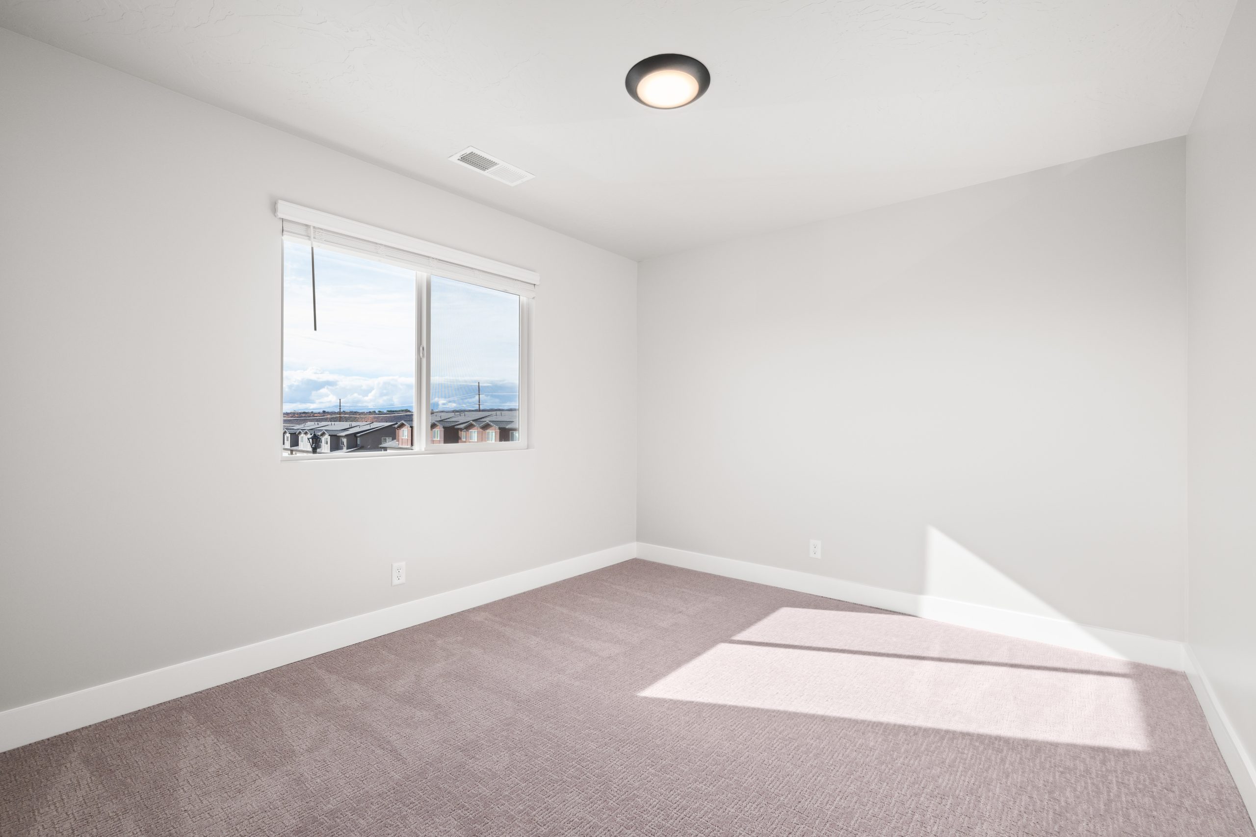 Bright upstairs bedroom with neutral carpet, large window, and natural light in the Sunrise townhome at Rise in Washington, Utah.