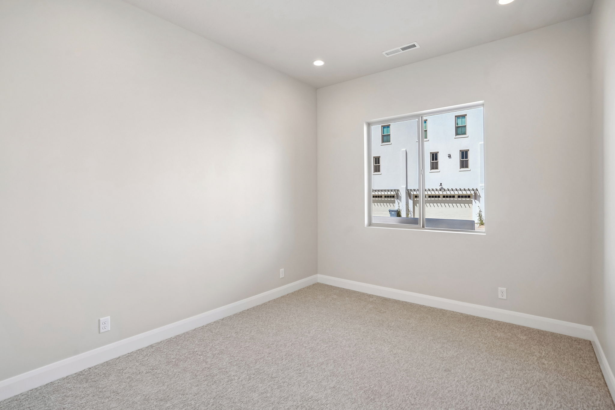 Spacious bedroom in the Pacific II at Desert Color featuring neutral carpeting, white walls, recessed lighting, and a window providing natural light.
