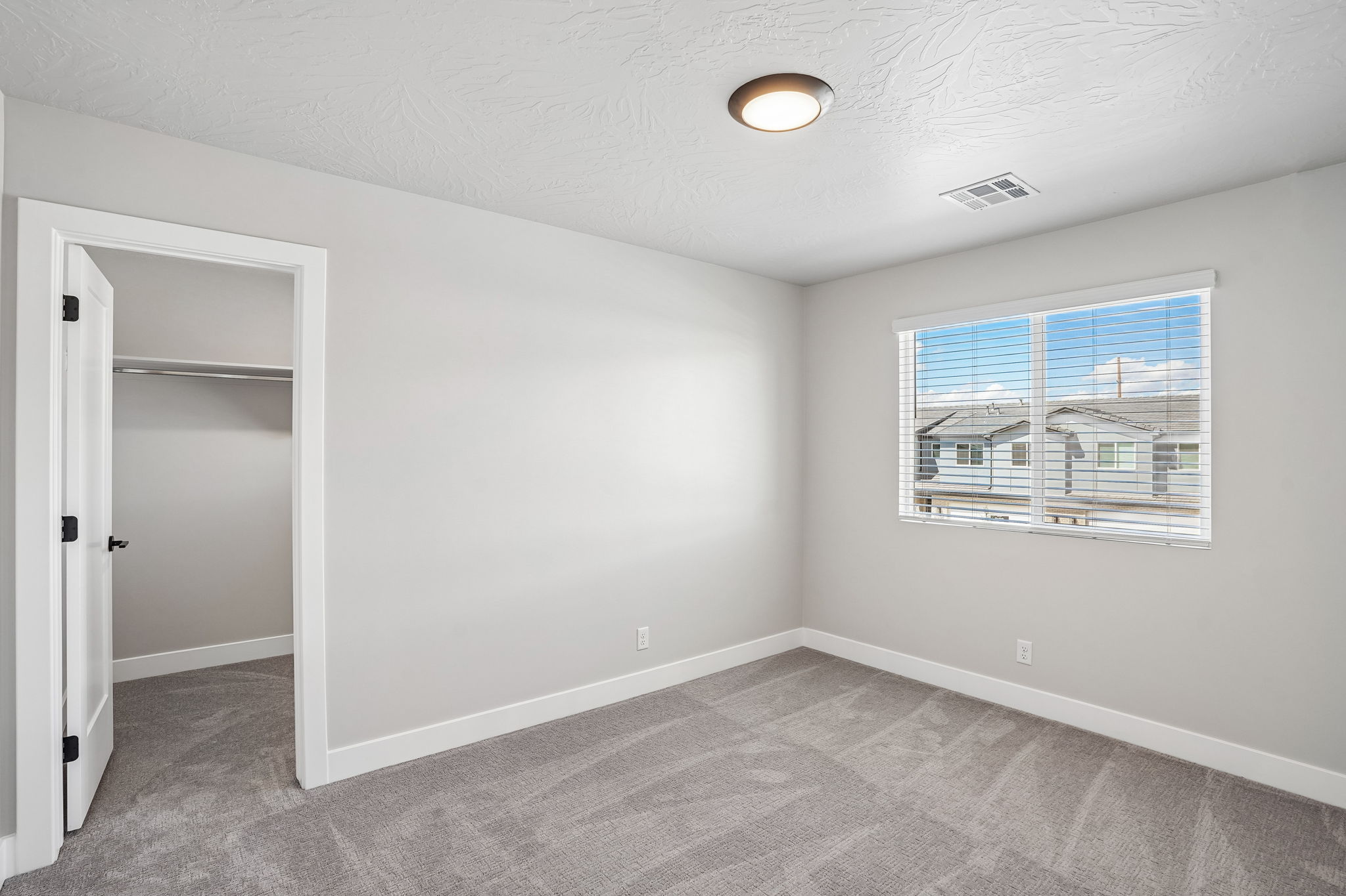 Bright bedroom in the Sunburst townhome at Rise by Cole West, featuring neutral carpet, a large window, and a spacious walk-in closet.