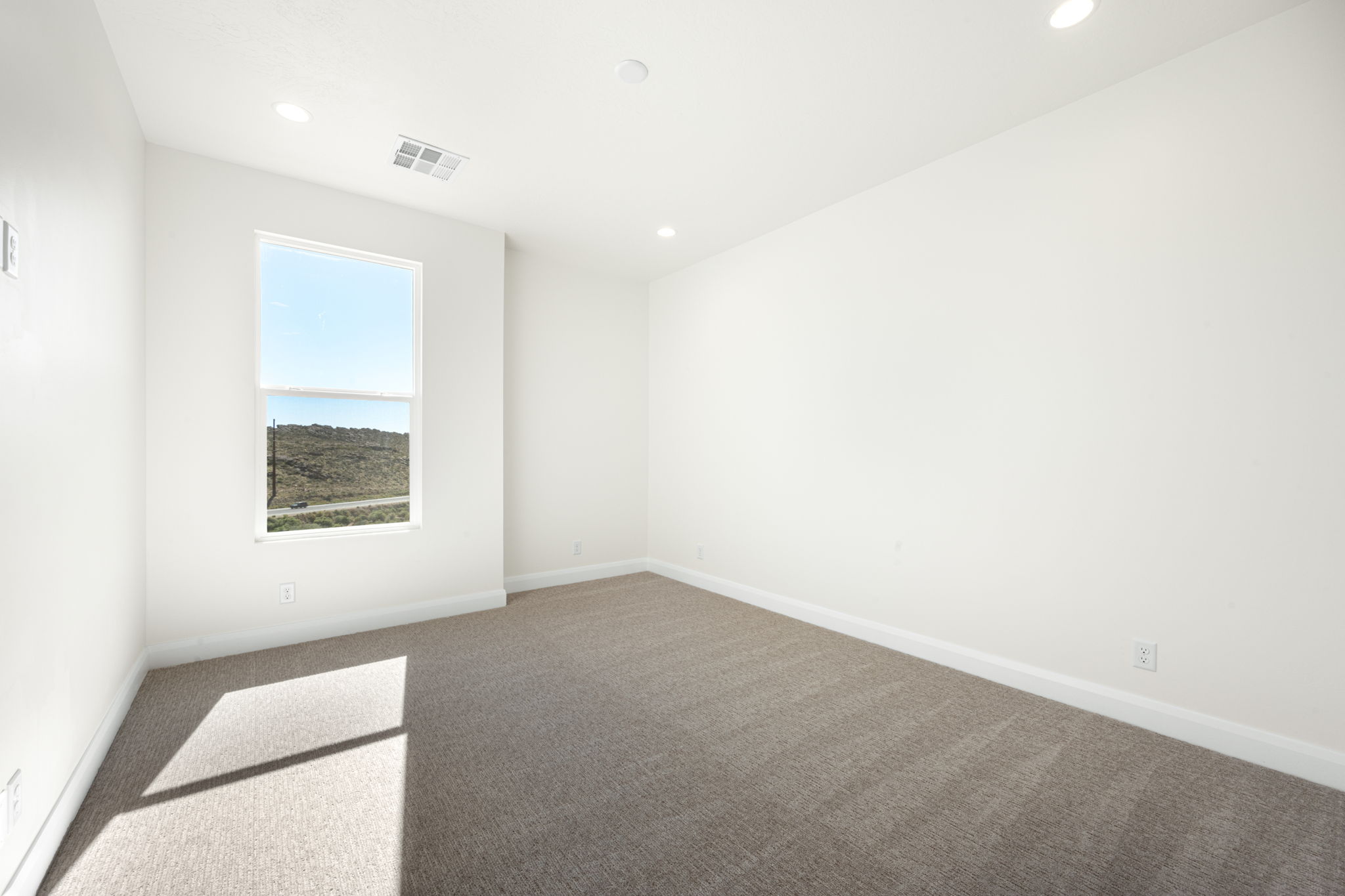 Spacious carpeted bedroom with recessed lighting, white walls, and a large window offering views of the Southern Utah desert.