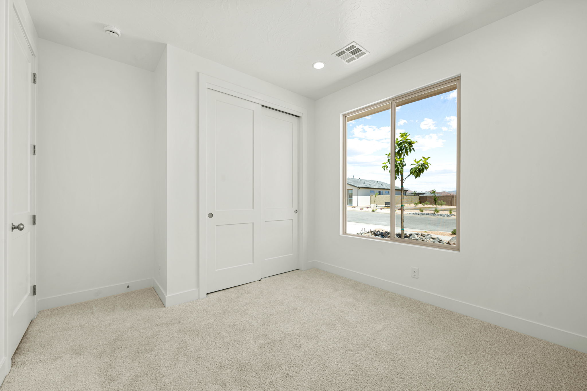Light-filled bedroom in the Basin floor plan by Cole West at Solis, featuring plush carpeting, sliding closet doors, and a large window.