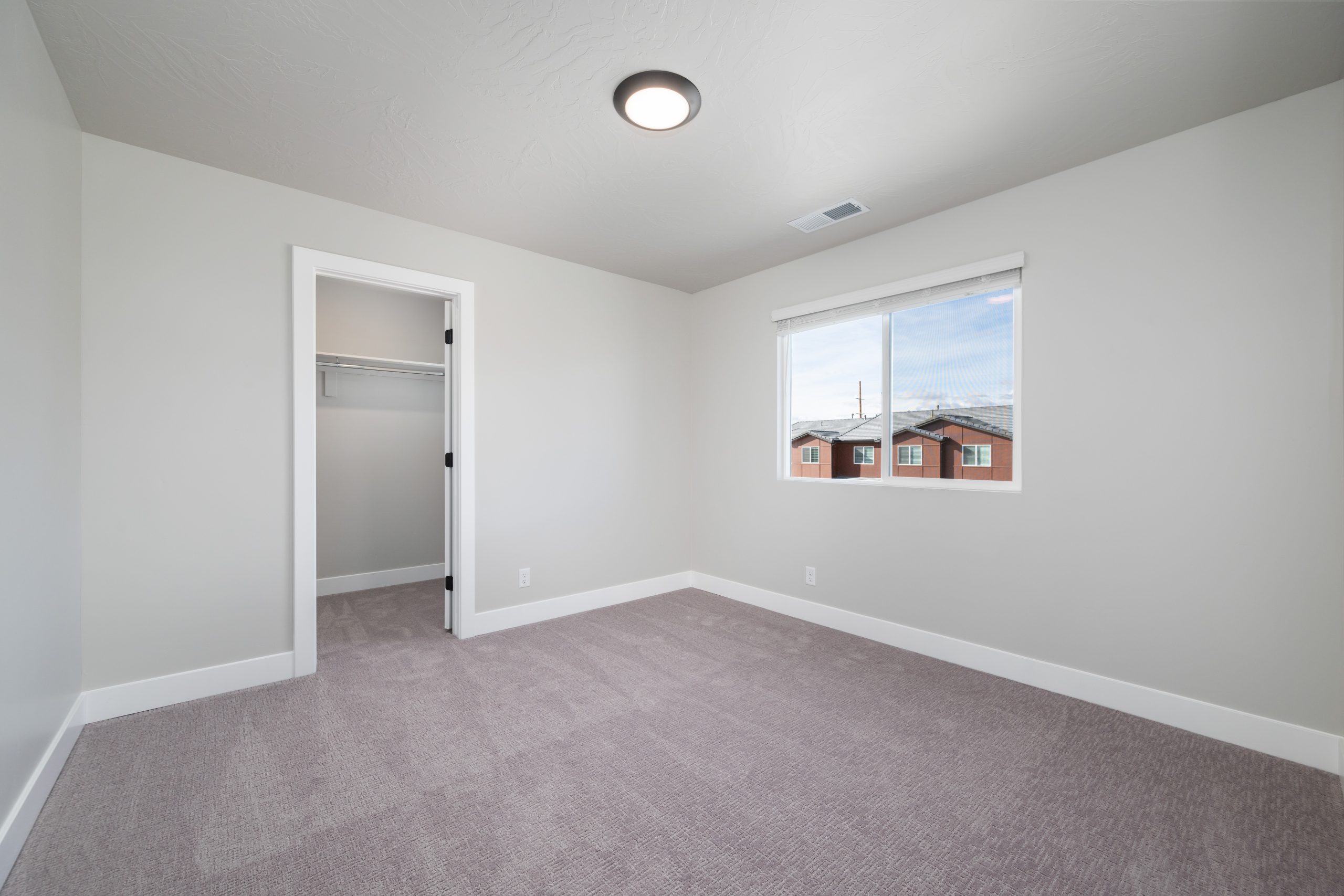 Spacious secondary bedroom featuring a walk-in closet, soft neutral carpeting, and natural light in the Sunrise floor plan by Cole West.