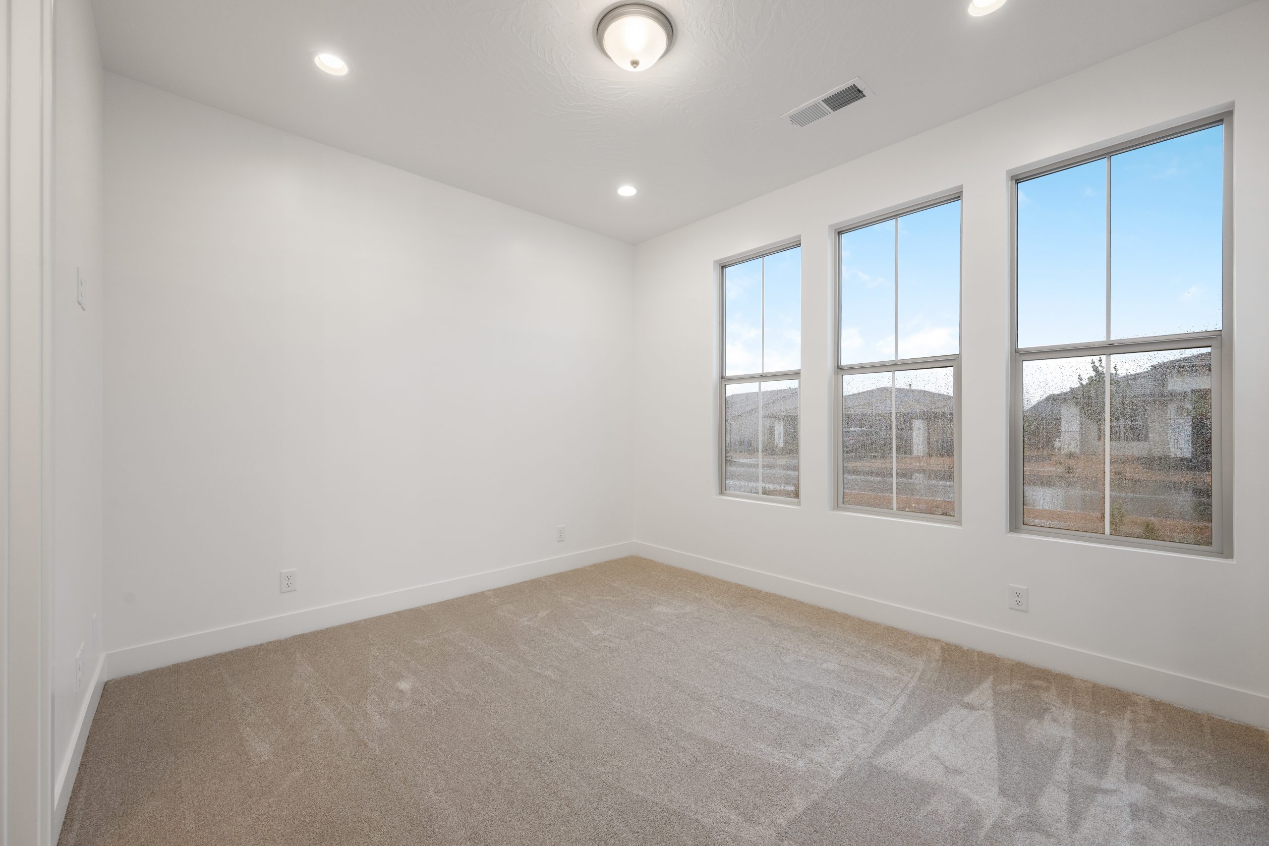 Spacious bedroom in the Mesa home by Cole West featuring three tall windows, soft neutral carpeting, and a bright, open interior.