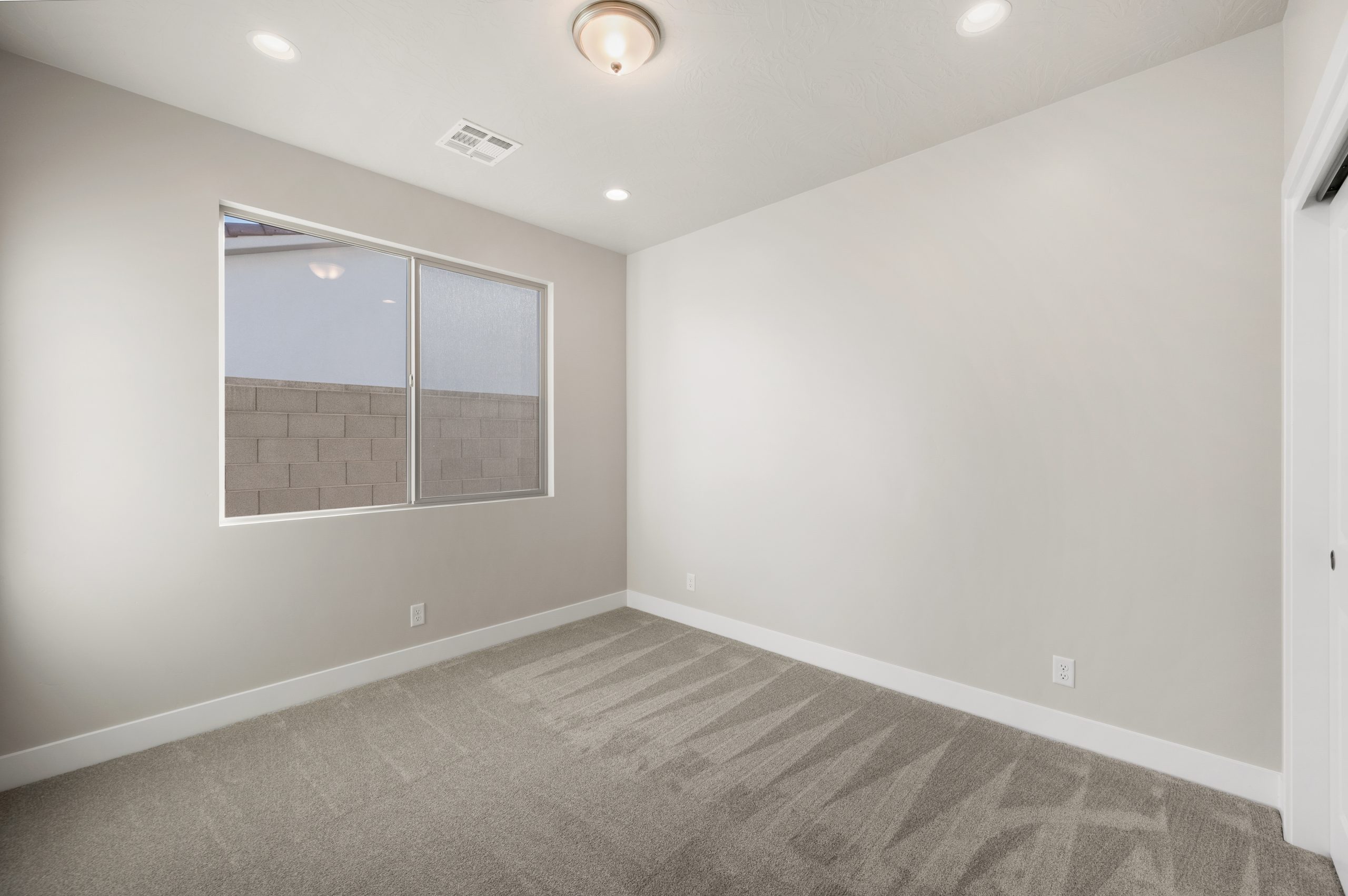 Modern bedroom with plush carpeting, neutral walls, and natural light in the Mojave home at Solis in Washington, Utah.