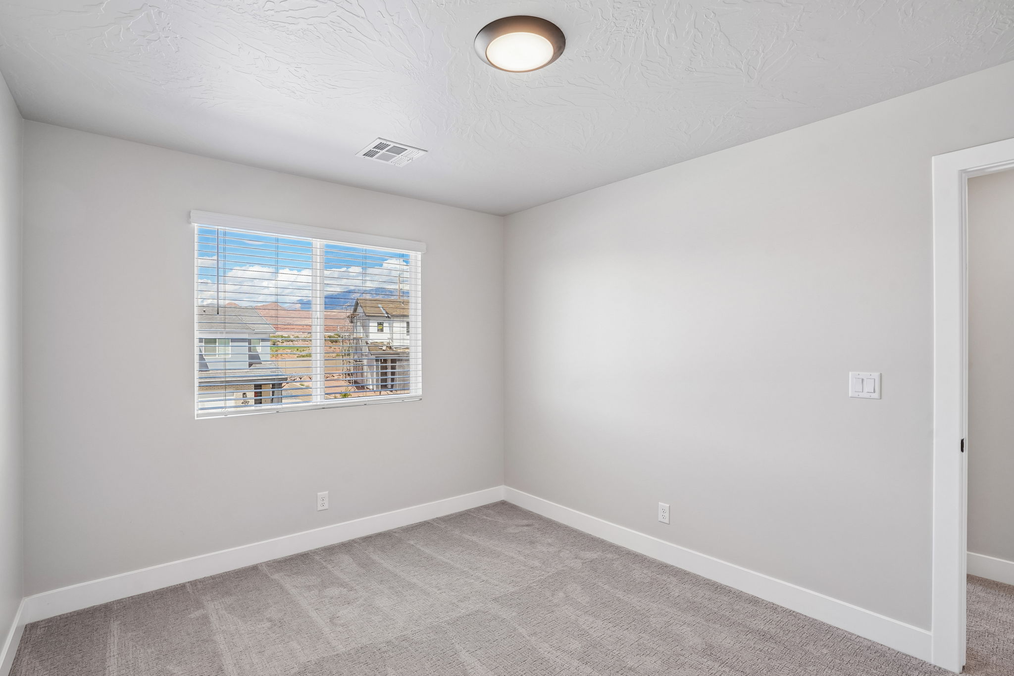 Sunburst floor plan bedroom in Washington, Utah, featuring soft gray carpet, white walls, and a window with scenic Southern Utah views.
