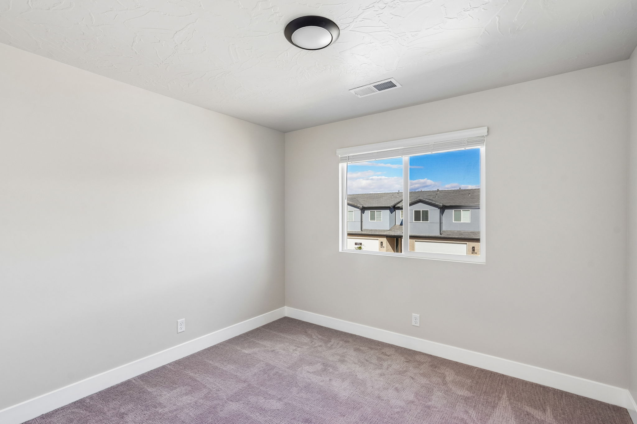 Comfortable bedroom featuring plush carpeting, a large window, and clean, modern finishes.