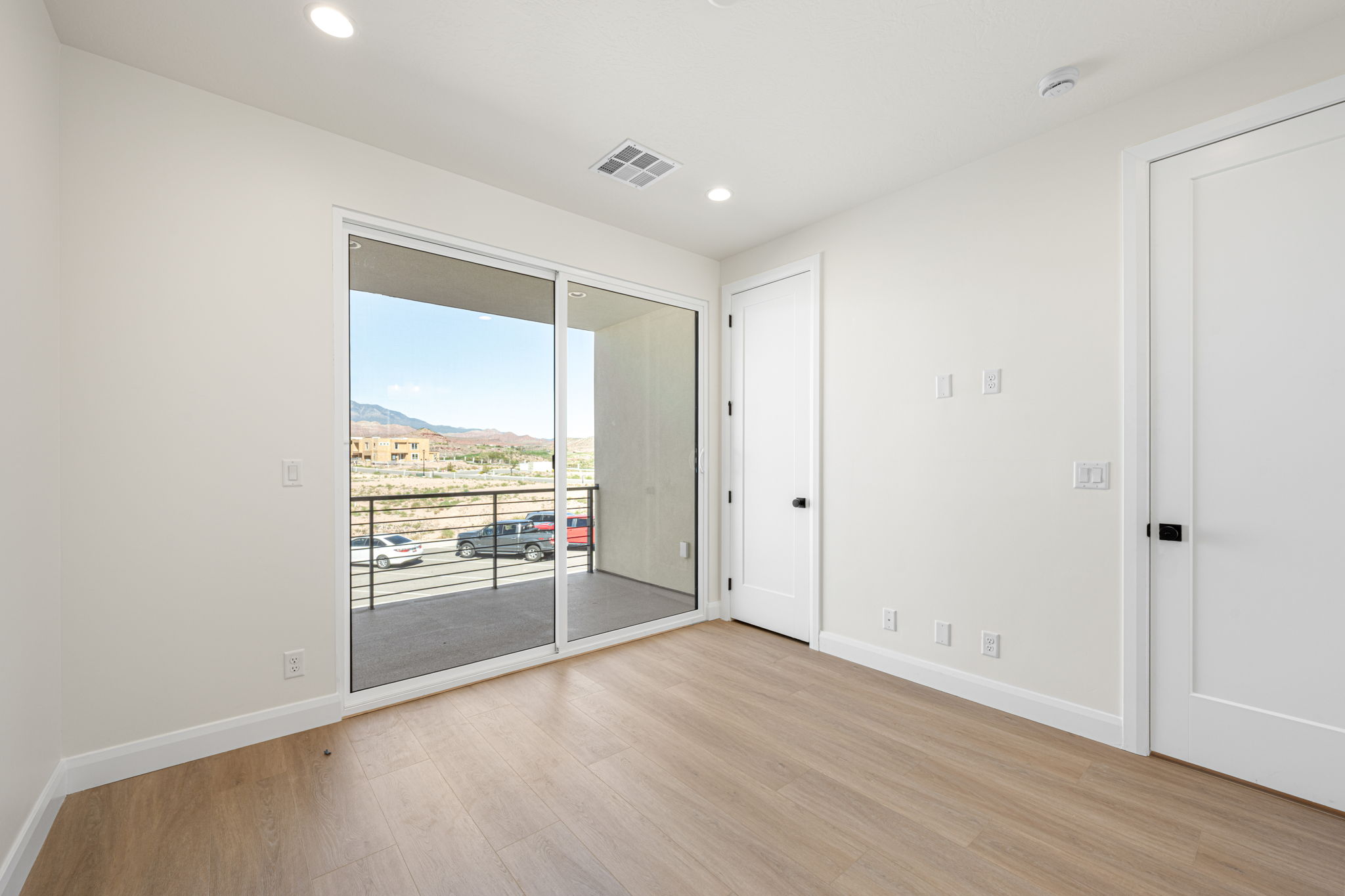 Modern bedroom featuring wood-look flooring and sliding glass doors opening to a private covered balcony with scenic views.