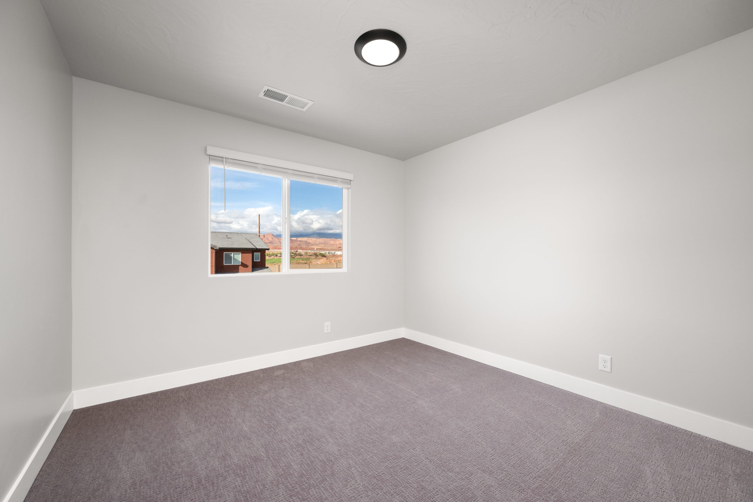 Modern upstairs bedroom with neutral finishes, plush carpeting, and Southern Utah red rock views in the Sunrise townhome at Rise.