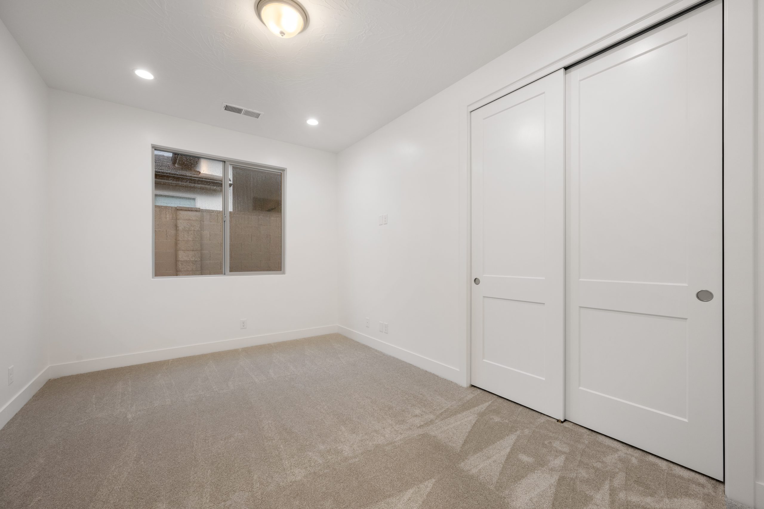 Modern bedroom in the Mesa floor plan at Solis by Cole West, featuring plush carpeting, a spacious closet with sliding doors, and neutral finishes.
