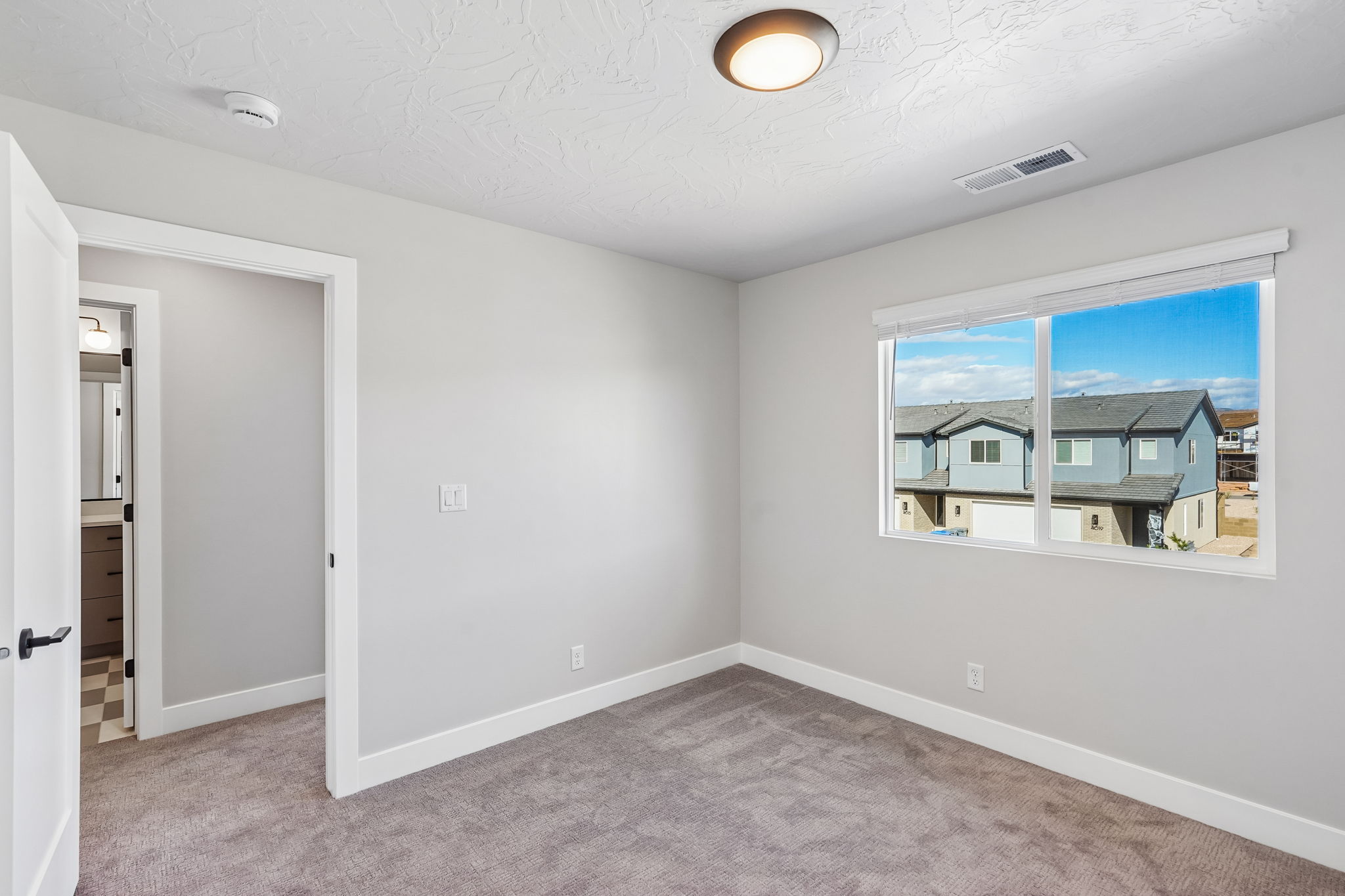 Comfortable bedroom with plush carpeting, a large window, and easy access to the hallway.