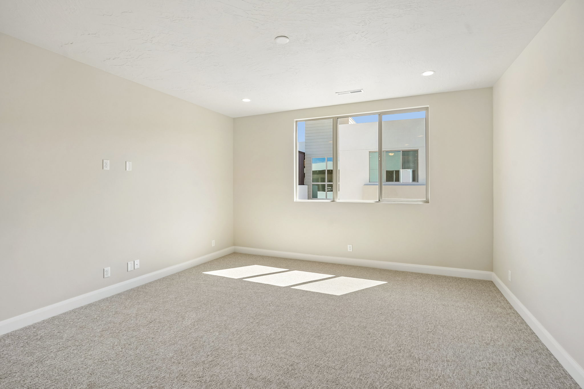 Spacious bedroom in the Pacific II by Cole West featuring a large window, neutral carpeting, and modern recessed lighting.