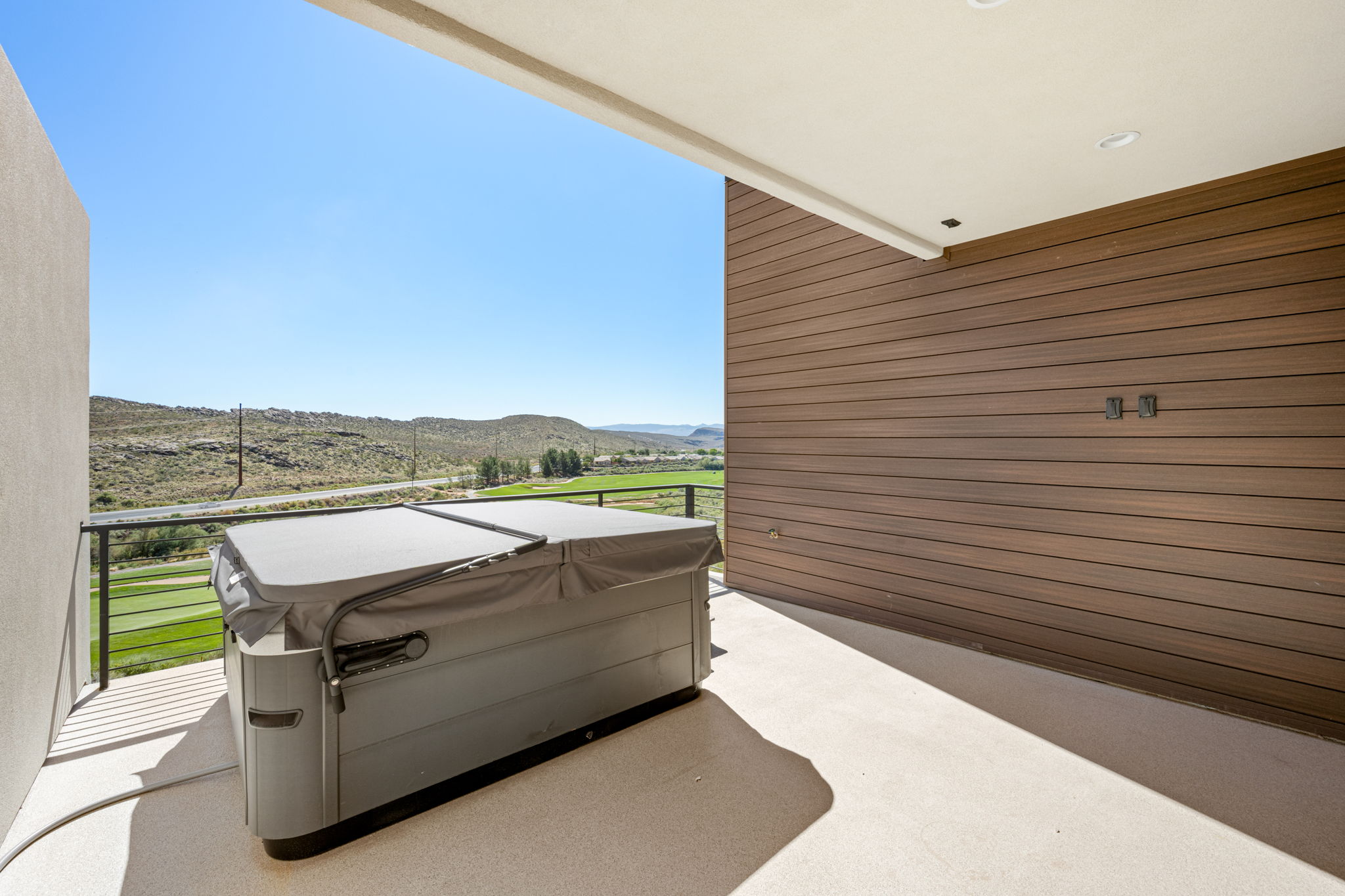 Private covered upper-level deck featuring a hot tub, modern wood-look siding, and panoramic views of the surrounding desert landscape.
