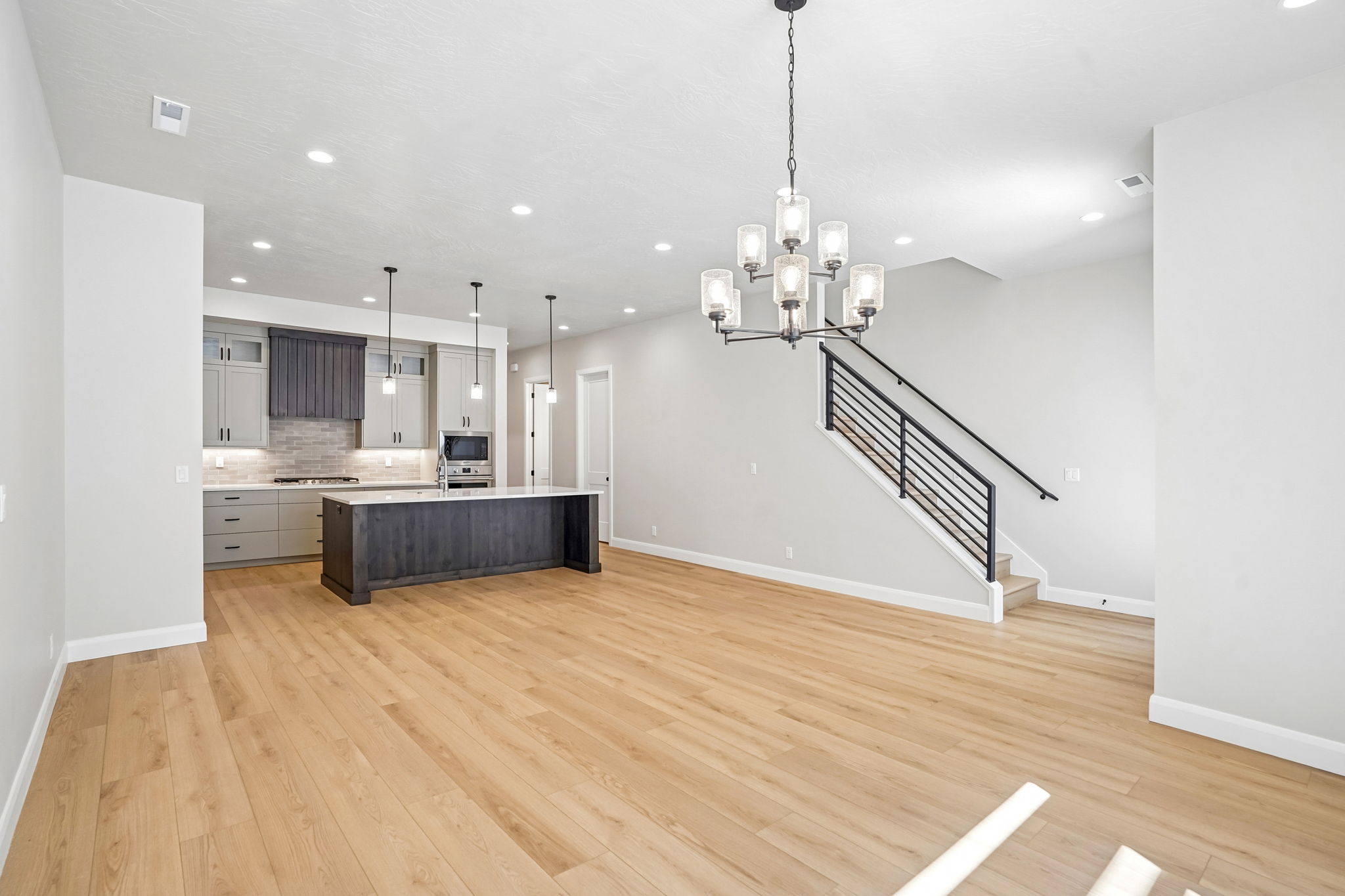Open-concept dining area in the Pacific II at Desert Color featuring light wood flooring, modern chandelier, spacious kitchen, and contemporary staircase.