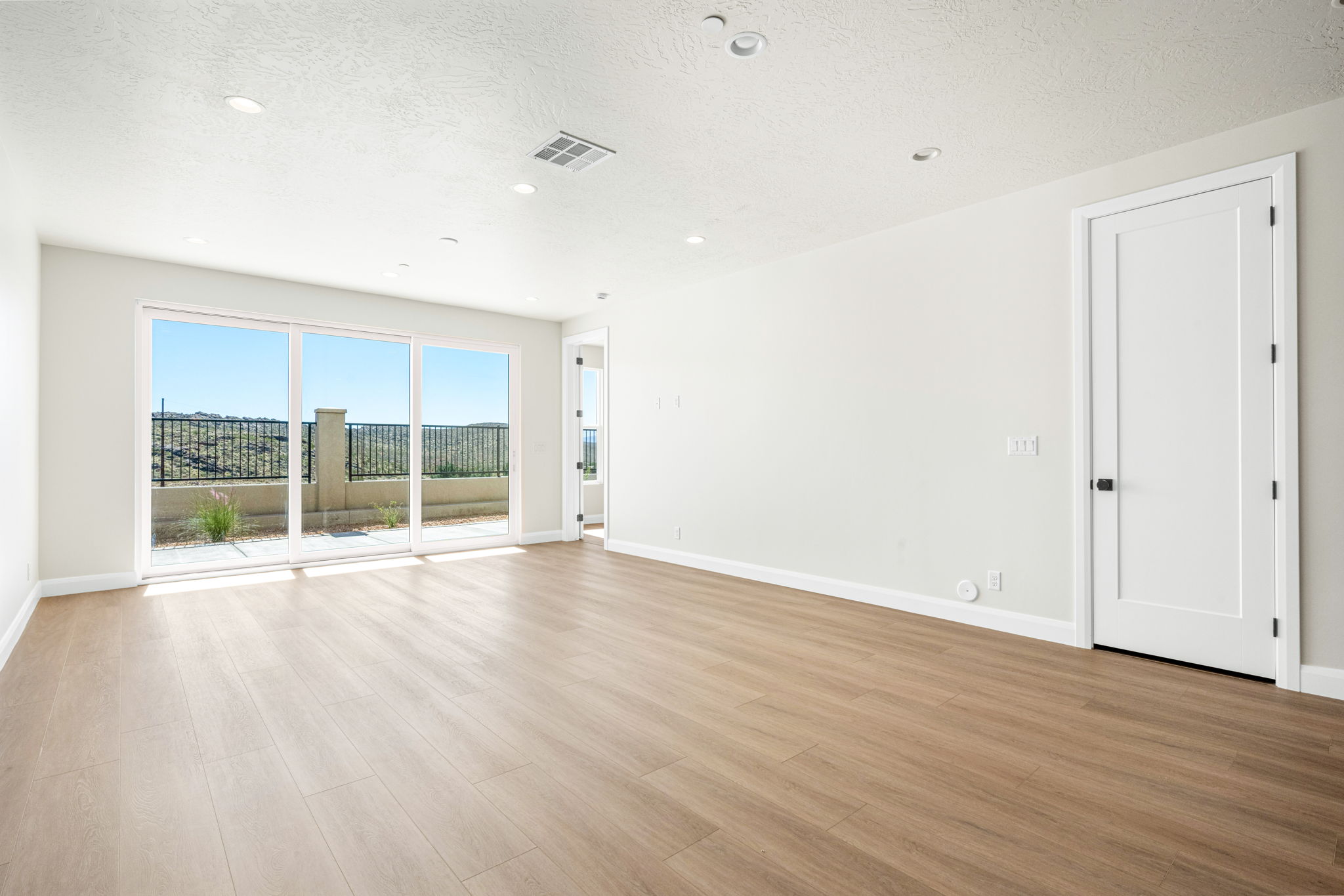 Spacious great room featuring wood-look flooring, recessed lighting, and large sliding glass doors leading to an outdoor patio.