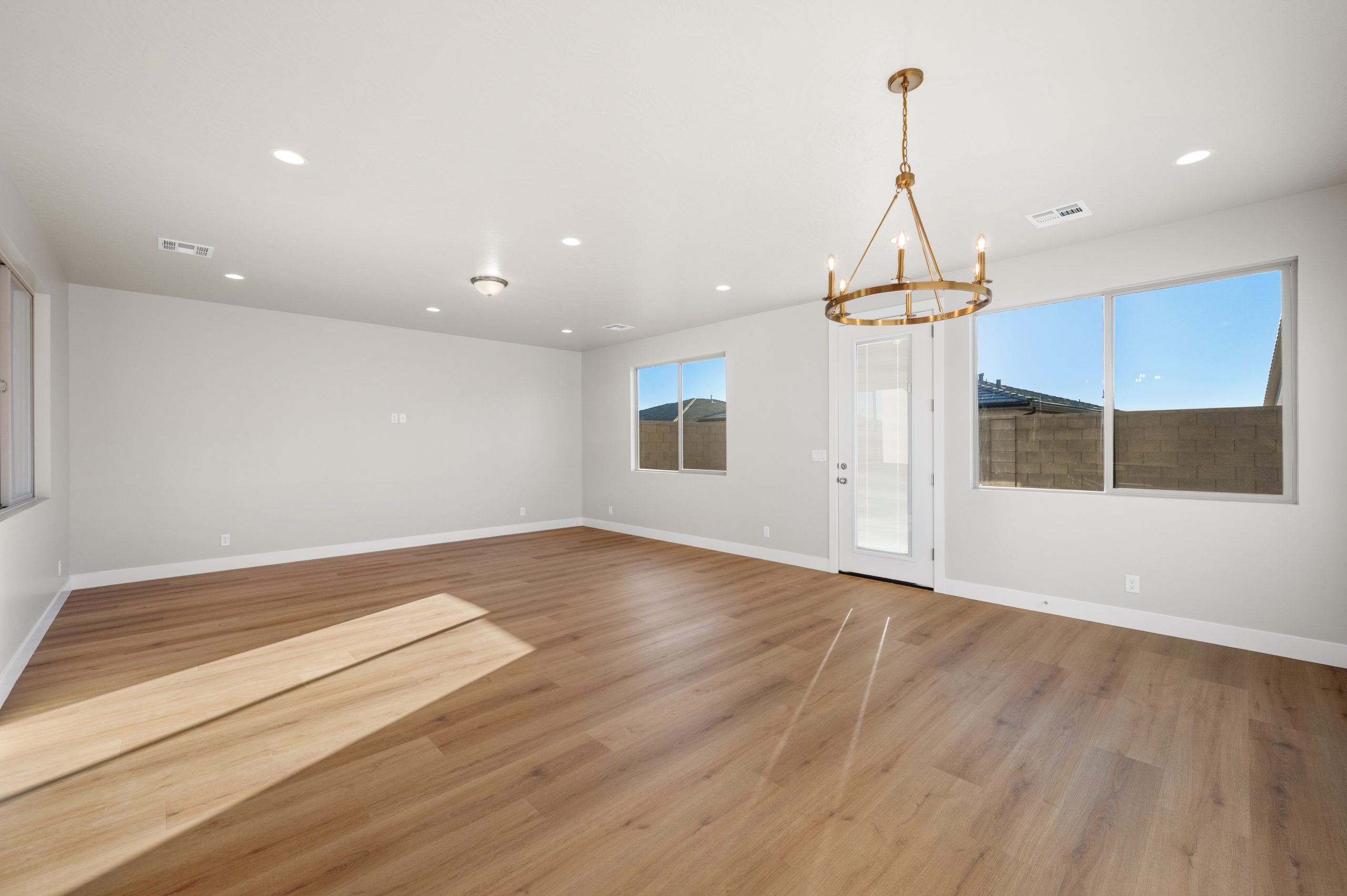 Spacious open-concept great room with wood-look flooring, large windows, and a modern chandelier in the Mojave floor plan at Solis by Cole West.
