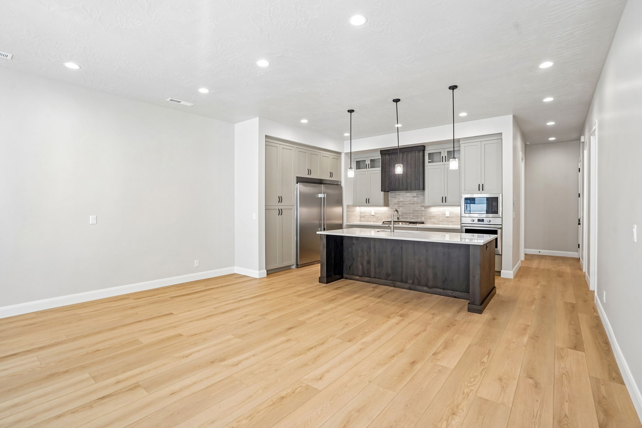 Open-concept great room in the Pacific II by Cole West featuring light wood flooring, a spacious kitchen island, stainless steel appliances, and modern finishes.
