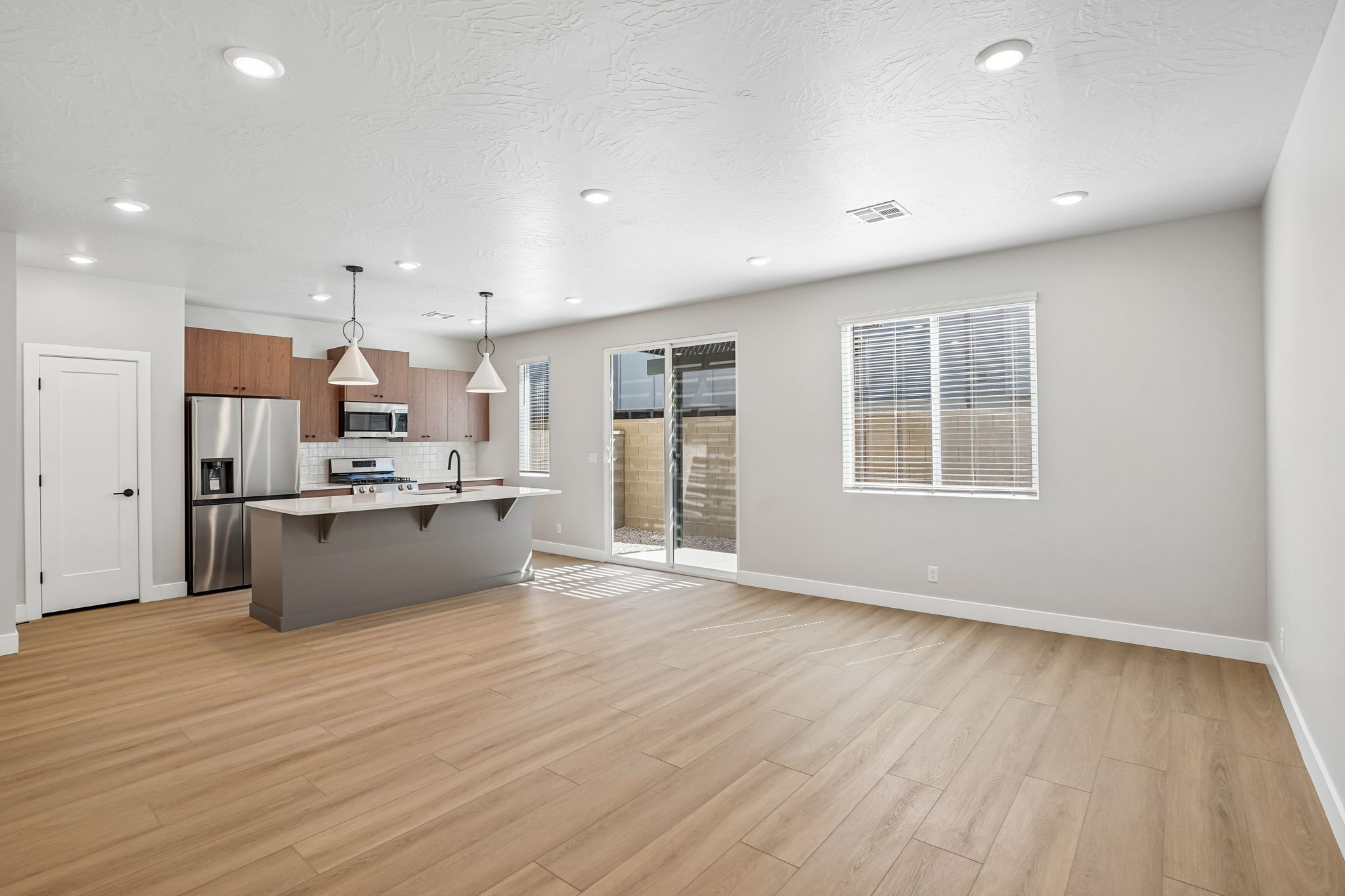 Open-concept great room in the Sunburst floor plan at Rise by Cole West, featuring wood-look flooring, natural light, and a modern kitchen.