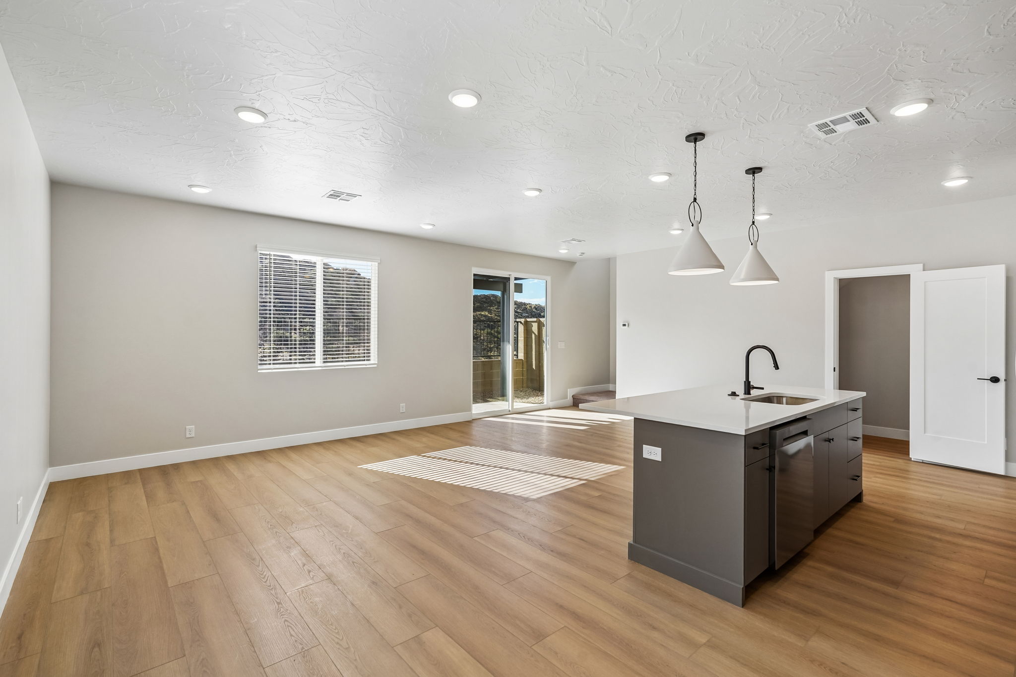 Bright, open-concept great room featuring wood-look flooring, a large kitchen island, and backyard access.