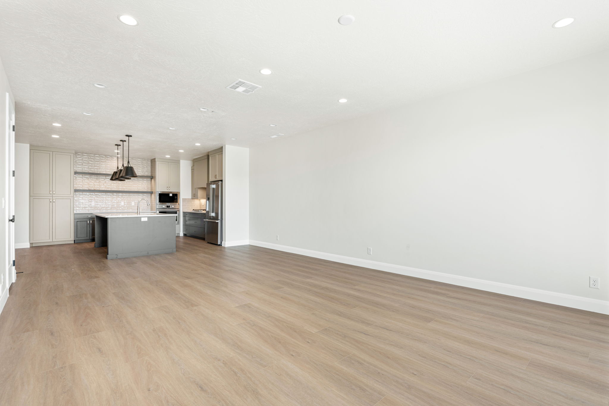 Open-concept living and dining area with modern wood-look flooring, recessed lighting, and a contemporary kitchen with a large island.