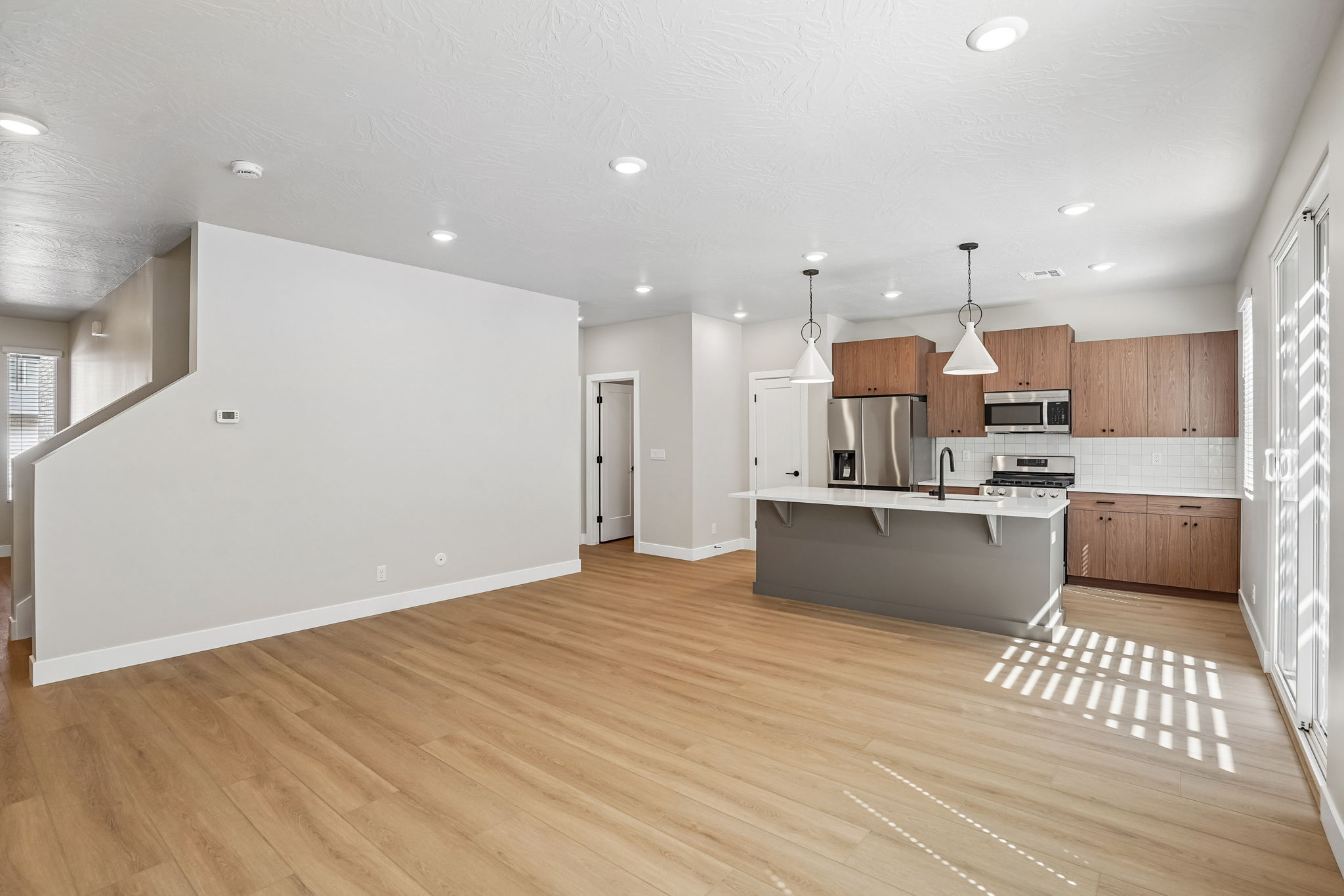 Open-concept great room in the Sunburst floor plan at Rise by Cole West, featuring wood-look flooring, natural light, and a modern kitchen.