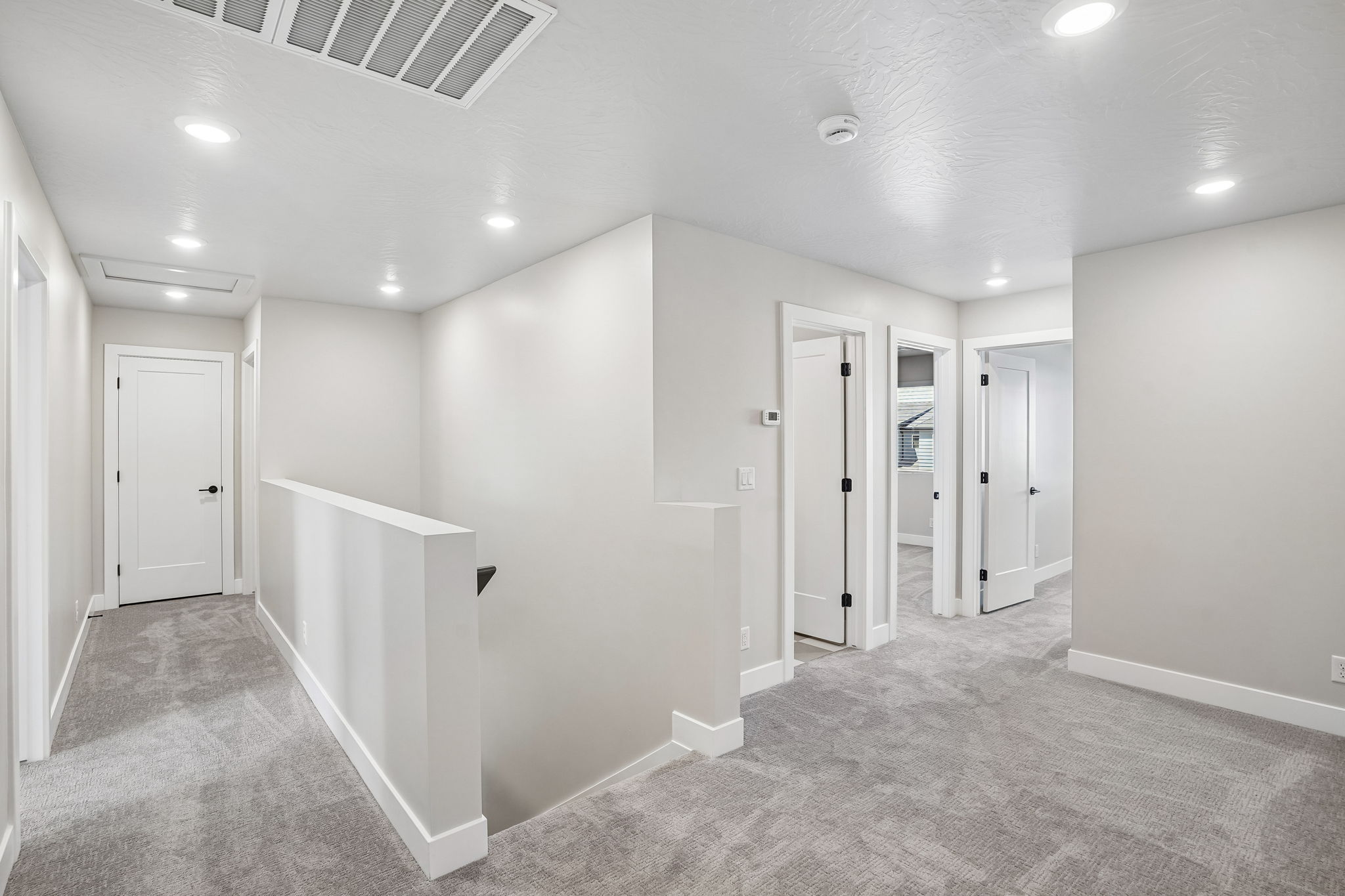 Upstairs hallway and loft area in the Sunburst townhome at Rise by Cole West, featuring soft carpeting, recessed lighting, and access to multiple bedrooms.