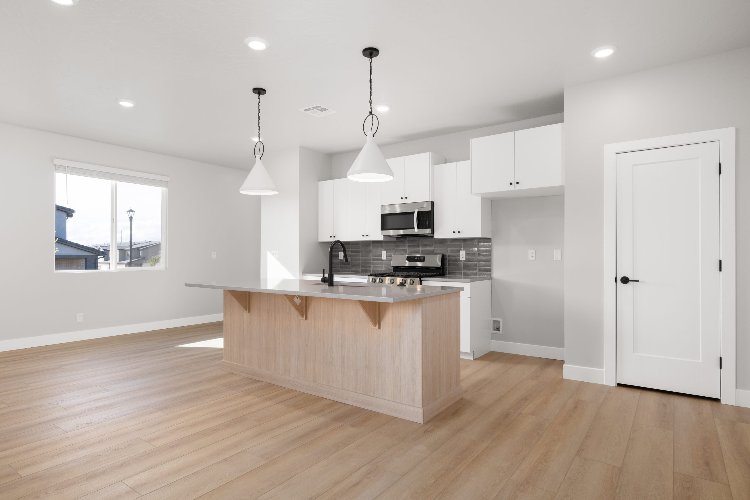 Contemporary kitchen featuring a large center island, white cabinetry, stainless steel appliances, and modern pendant lighting in the Sunrise townhome at Rise.