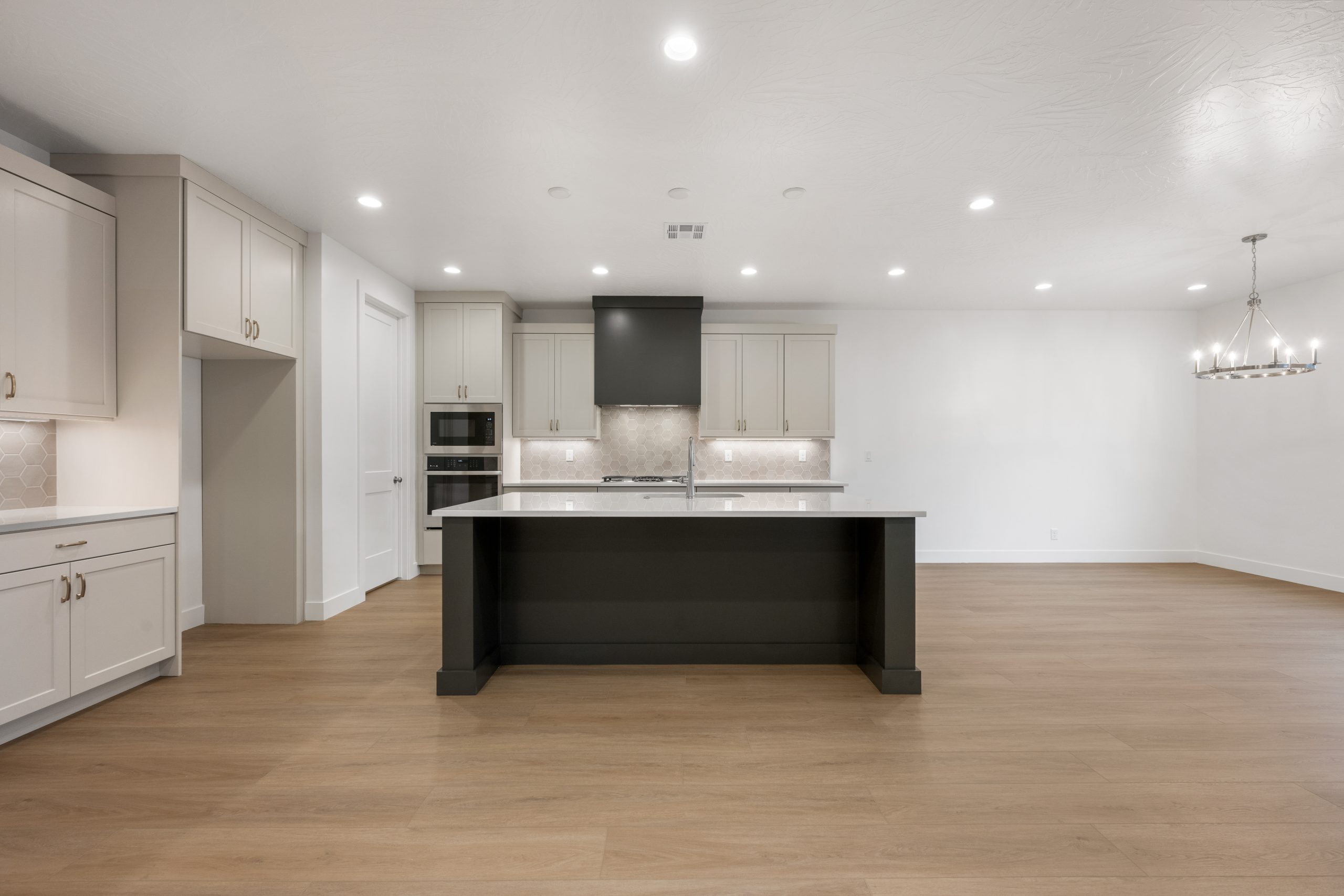 Modern kitchen in the Mesa floor plan by Cole West featuring a large dark kitchen island, white shaker cabinets, hexagon tile backsplash, and pendant lighting.