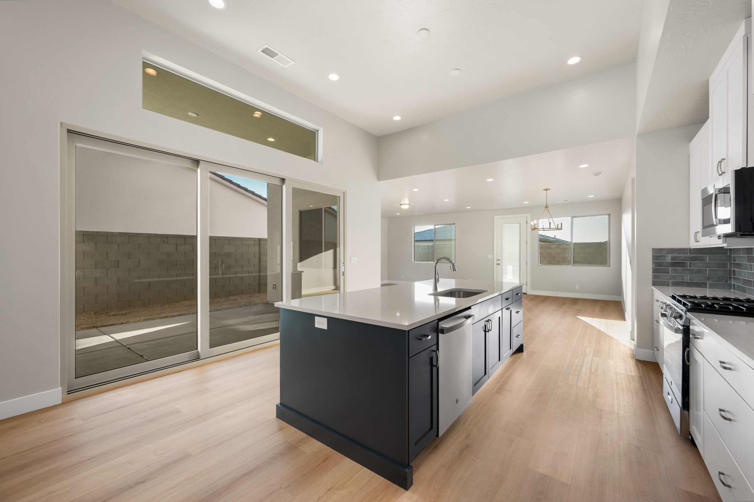 Spacious Mojave kitchen with a contrasting dark island, quartz-look countertops, and sliding glass doors leading to the patio at Solis in Washington, Utah.