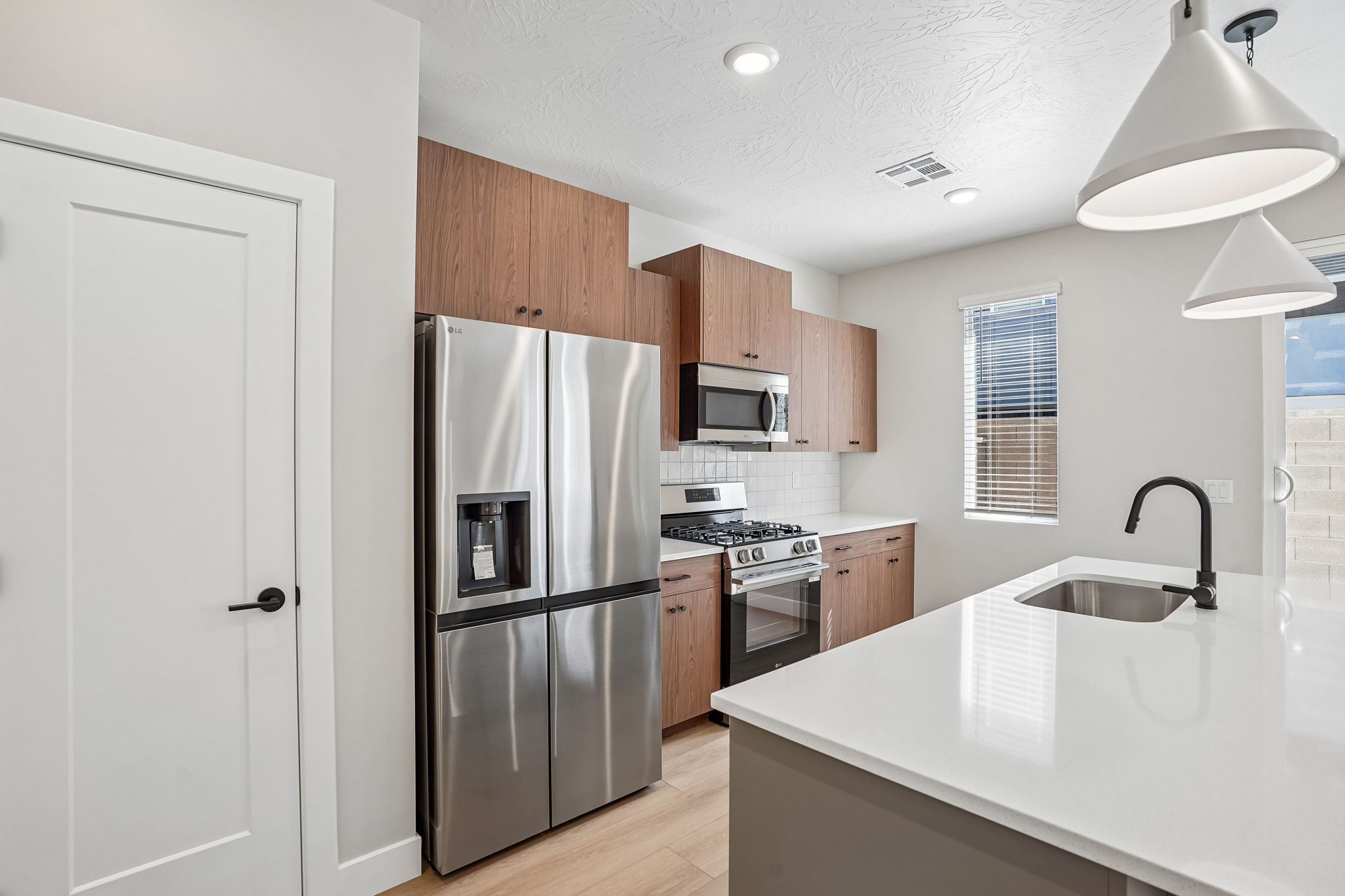 Modern kitchen in the Sunburst townhome by Cole West, featuring warm wood cabinetry, stainless steel appliances, and a spacious white island.