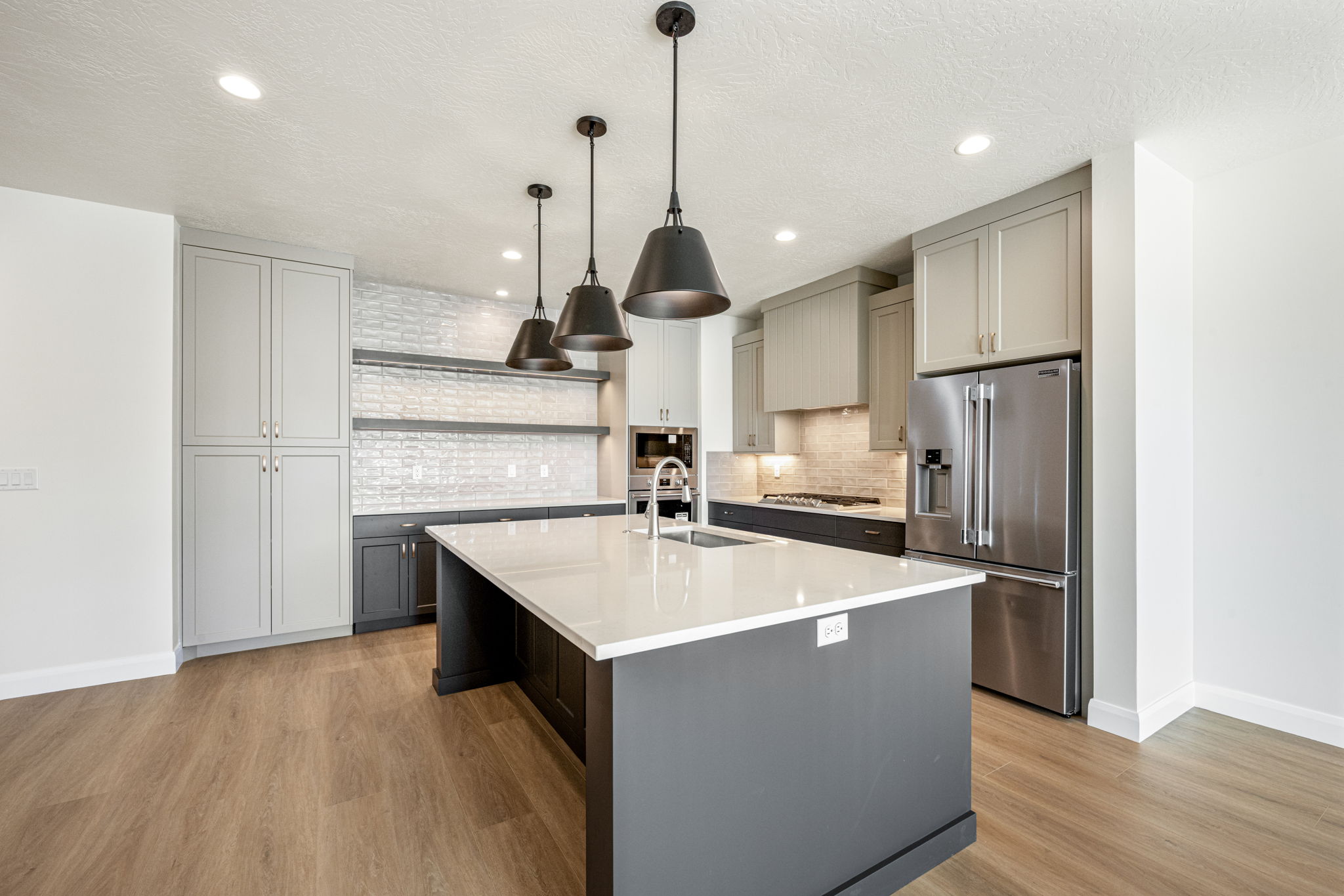 Contemporary kitchen featuring a large island, white quartz-style countertops, gray cabinetry, stainless steel appliances, and pendant lighting.