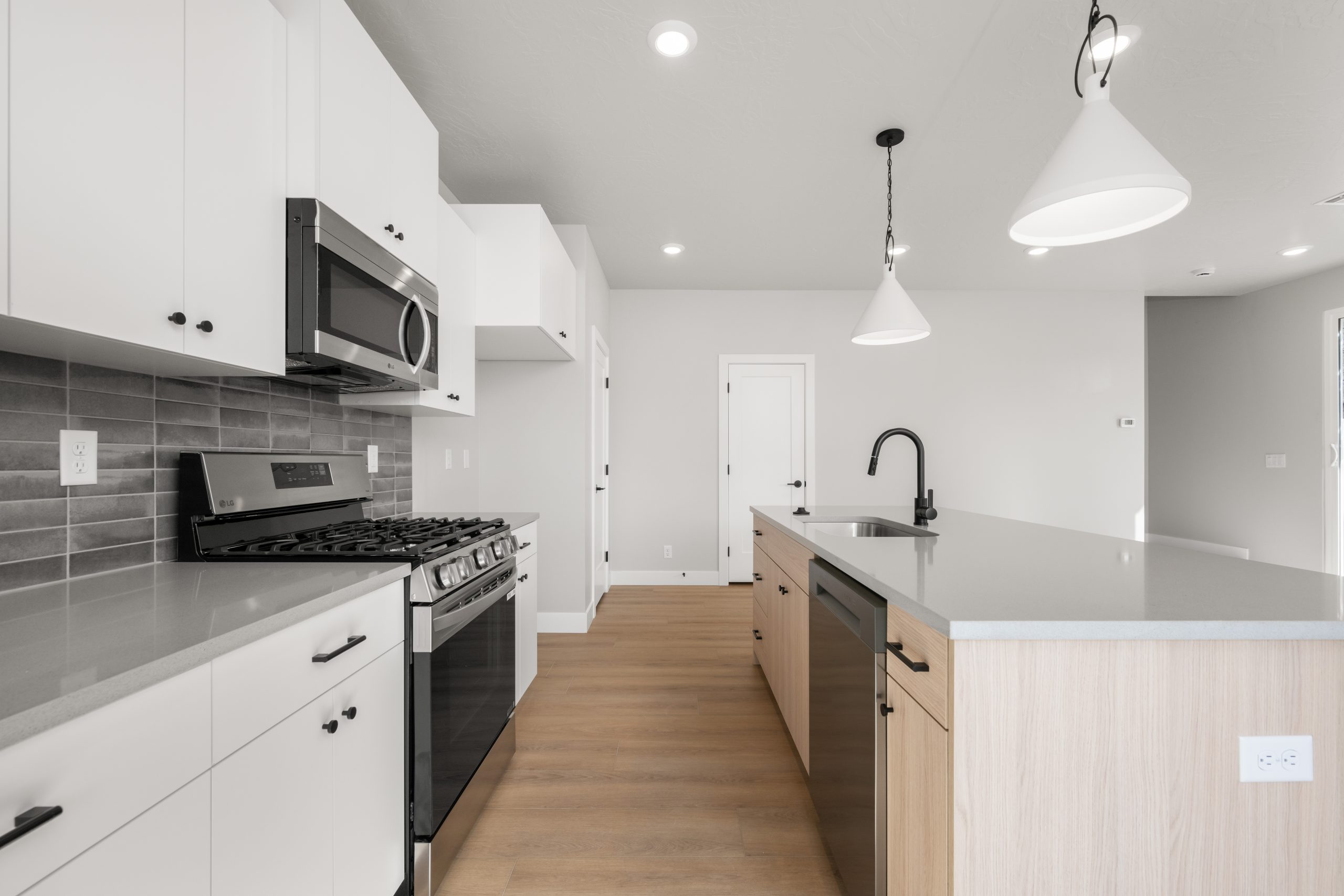 Stylish kitchen with quartz-look countertops, light wood island cabinetry, black fixtures, and stainless steel appliances in the Sunrise townhome in Washington, Utah.