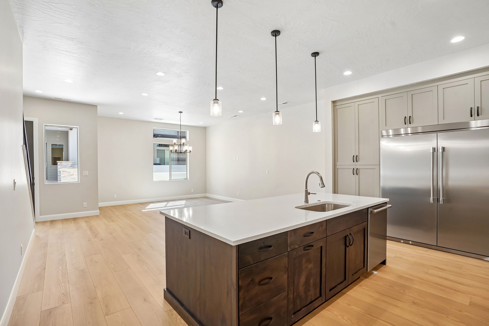 Open-concept kitchen and living area in the Pacific II by Cole West featuring a large kitchen island, stainless steel refrigerator, modern cabinetry, and natural wood flooring.
