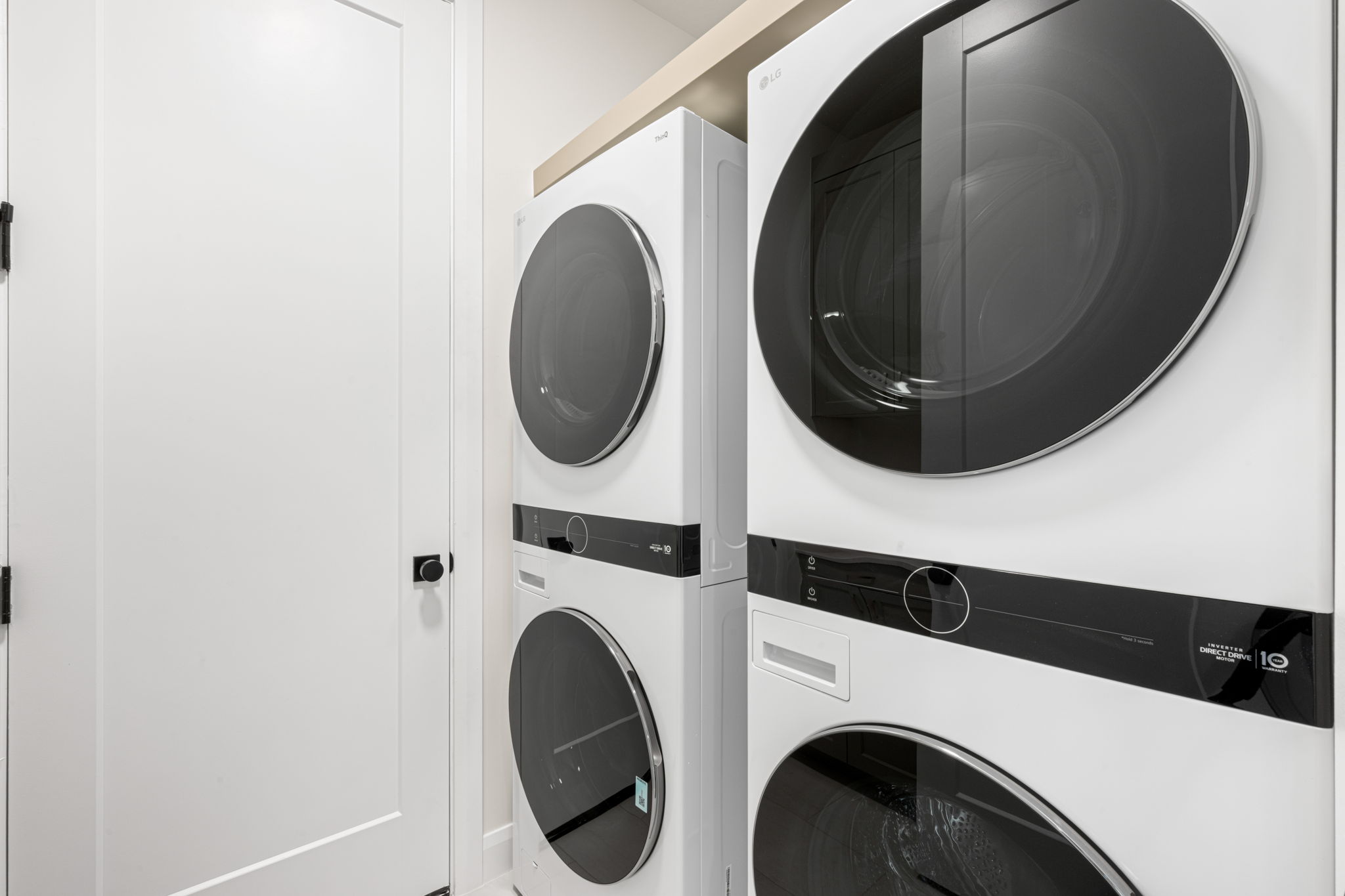 Laundry room featuring two sets of stacked washers and dryers with sleek black glass doors and white finishes.