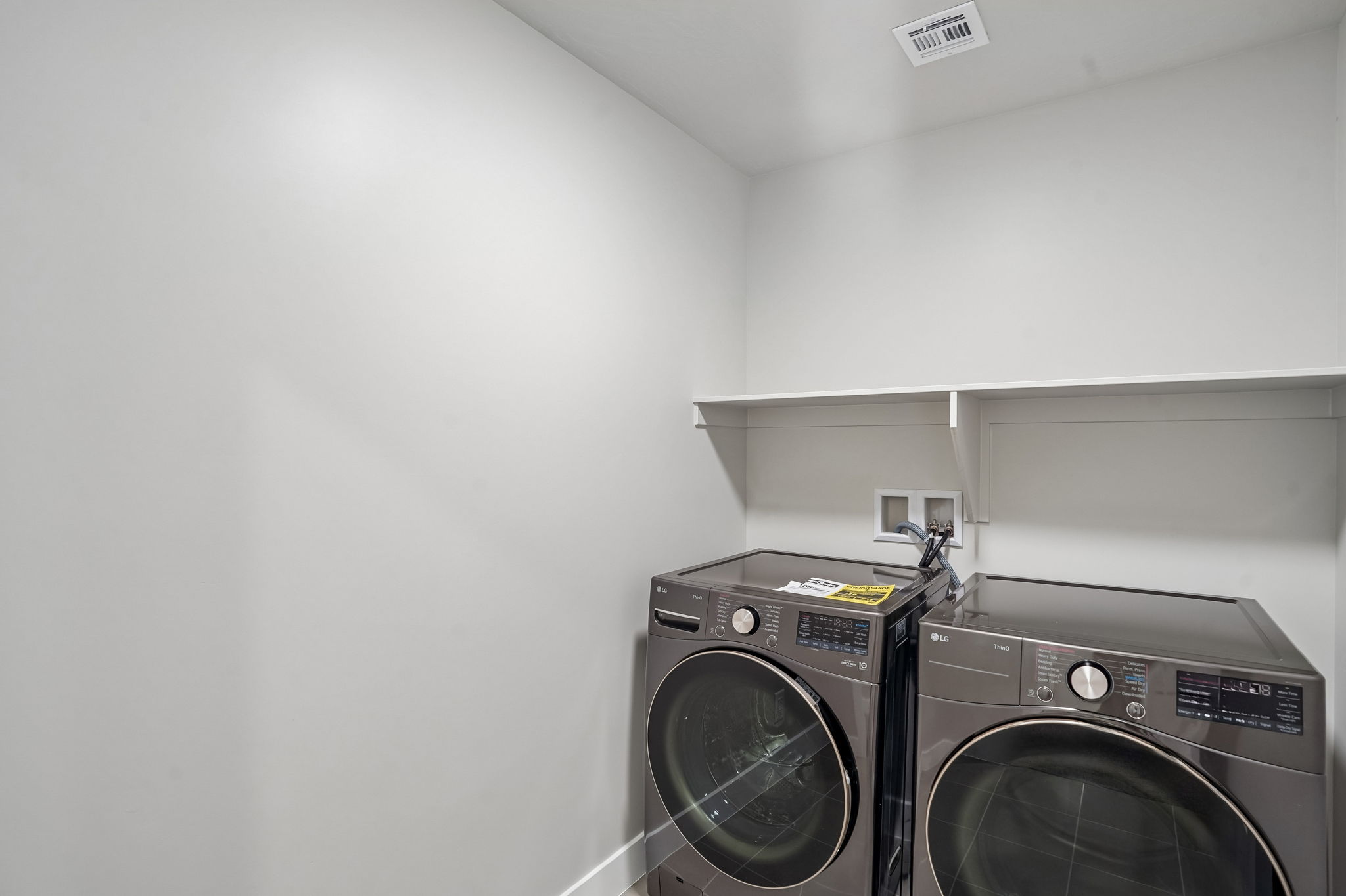 Dedicated laundry room in the Sunburst townhome at Rise by Cole West, featuring a front-loading washer and dryer with overhead storage shelving.
