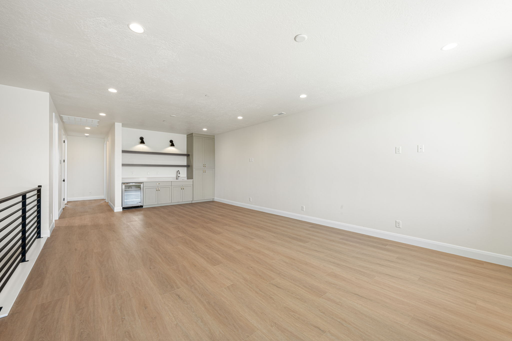 Spacious upstairs loft featuring wood-look flooring, recessed lighting, and a built-in wet bar with cabinetry and a beverage refrigerator.