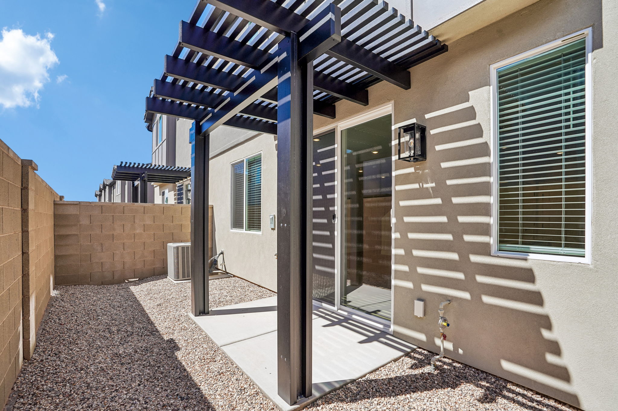Private outdoor patio at the Sunburst townhome by Cole West, featuring a modern pergola, sliding glass door, and low-maintenance landscaping.