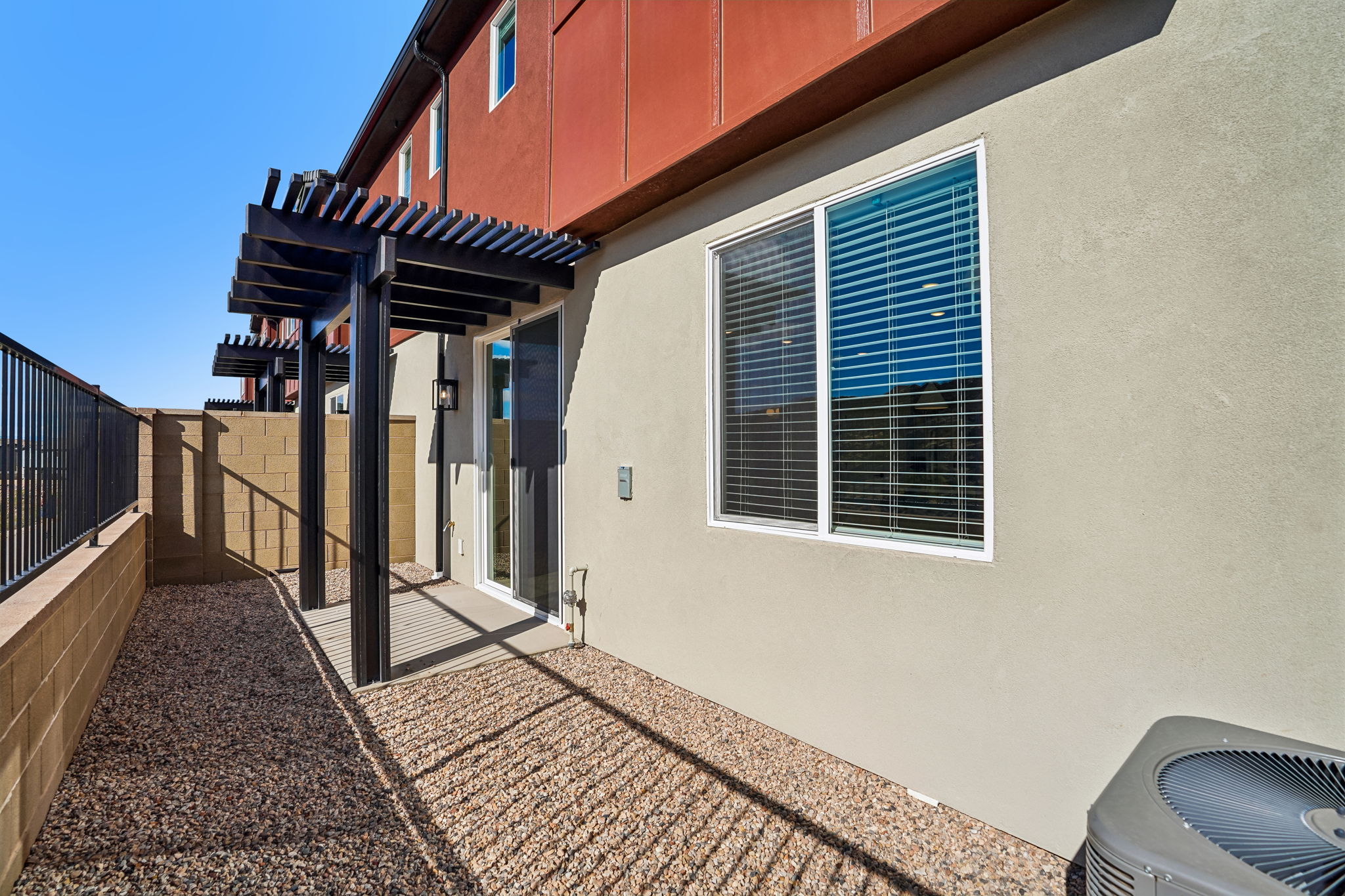 Low-maintenance outdoor patio featuring a pergola, gravel landscaping, and sliding glass door access.