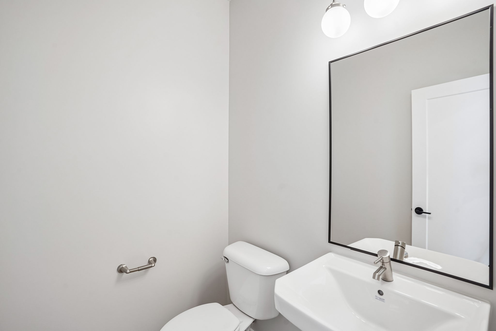 Modern powder bathroom in the Sunburst floor plan at Rise by Cole West, featuring a white pedestal-style sink, black-framed mirror, and contemporary fixtures.