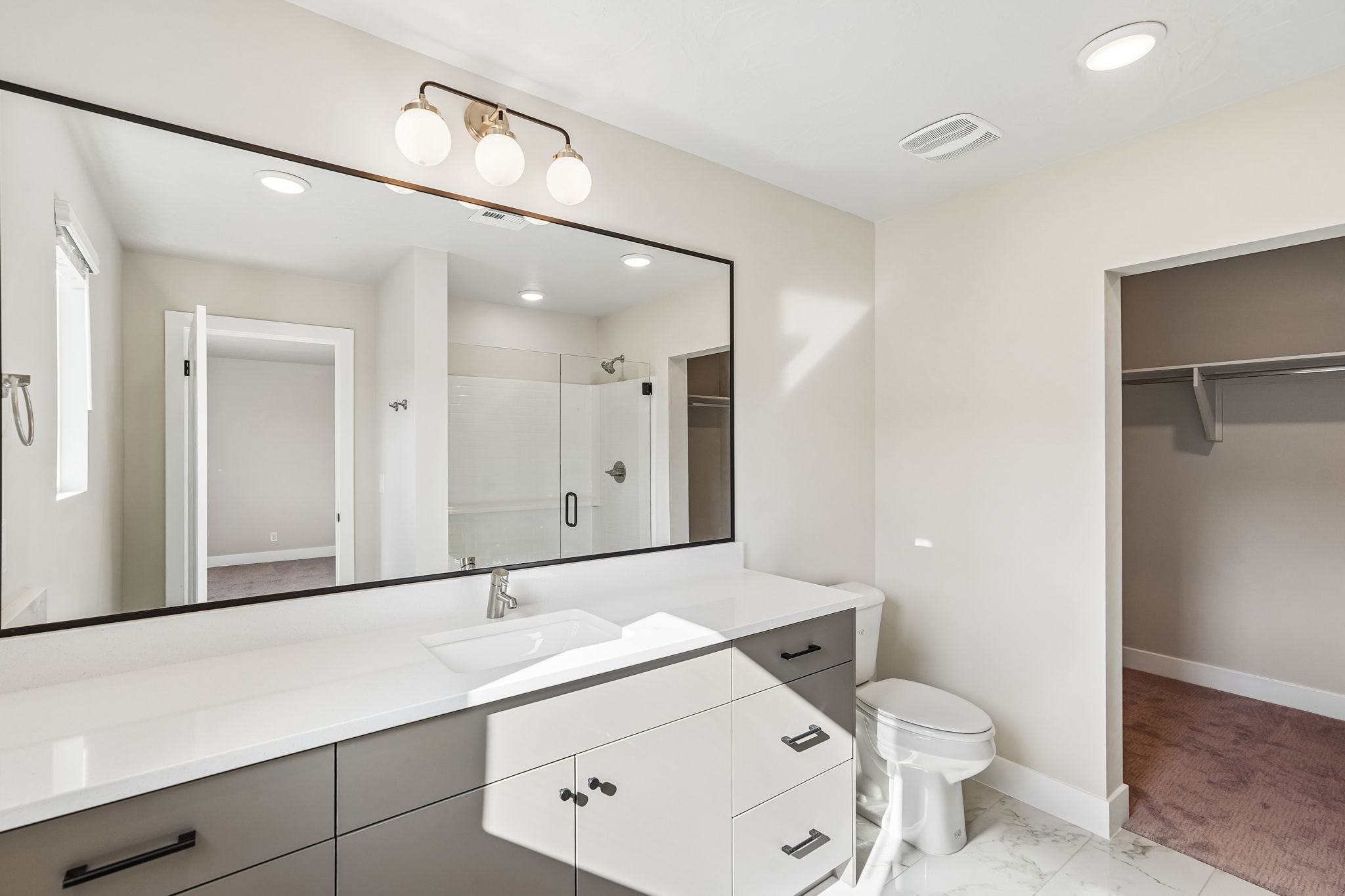 Modern primary bathroom featuring an extended vanity, walk-in shower, and access to the walk-in closet.