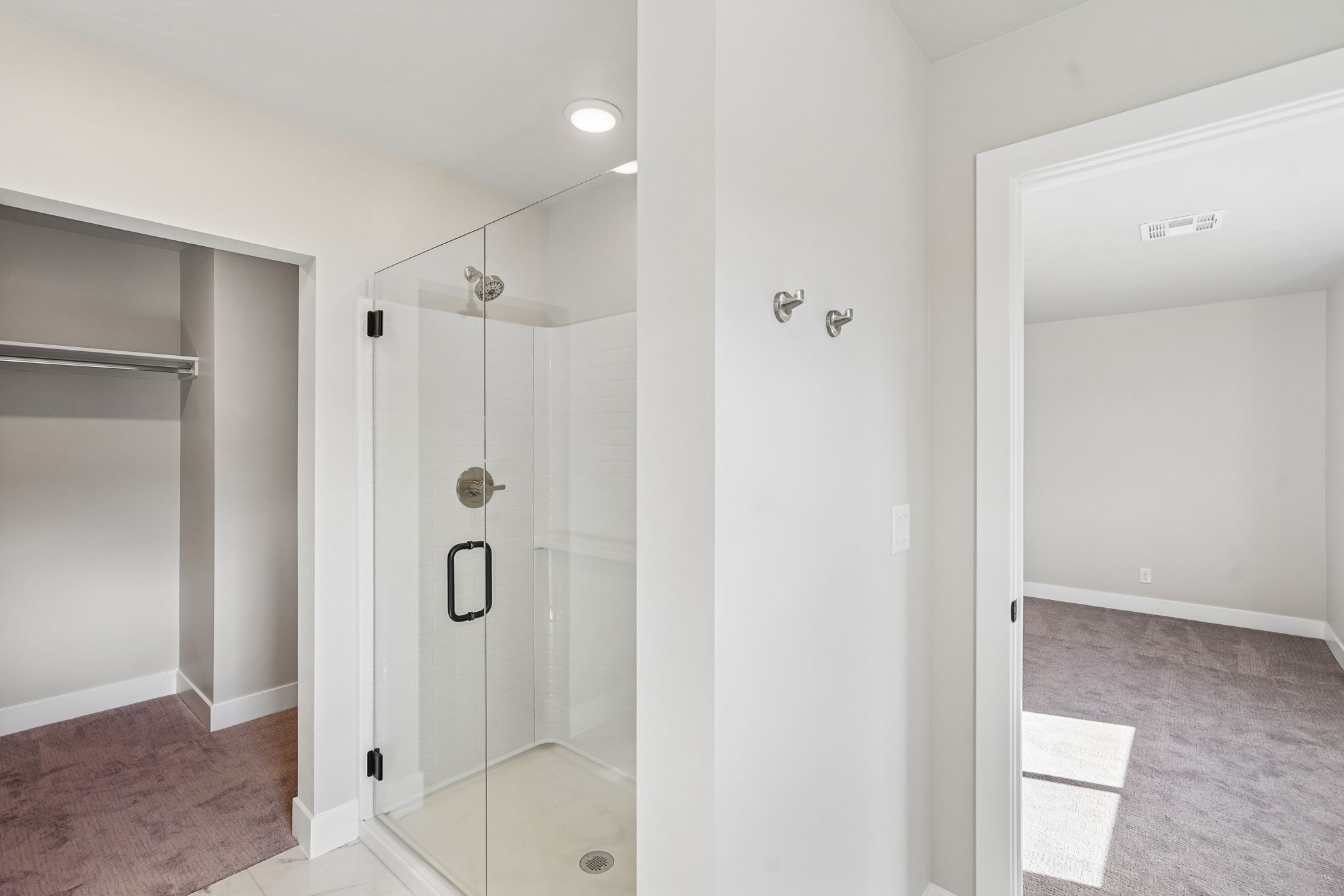Beautiful glass-enclosed shower with white tile and convenient access to the primary closet.