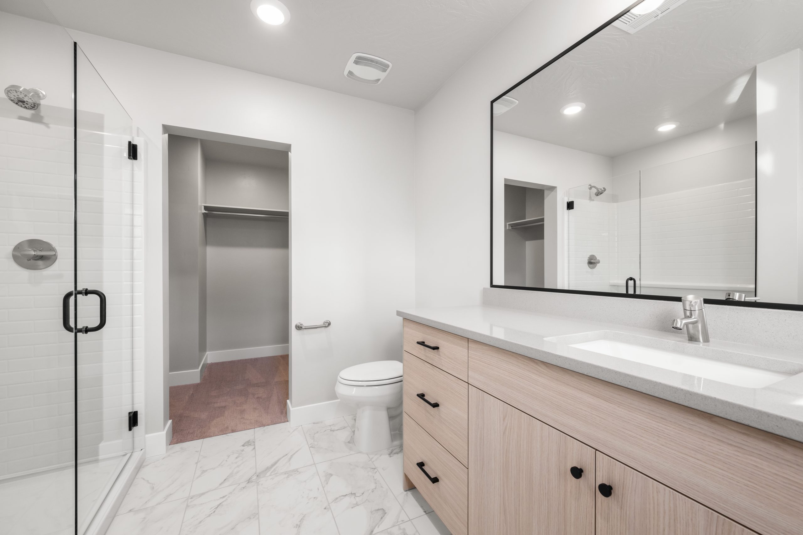 Spacious primary bathroom featuring a glass-enclosed walk-in shower, light wood vanity, and walk-in closet in the Sunrise floor plan by Cole West.