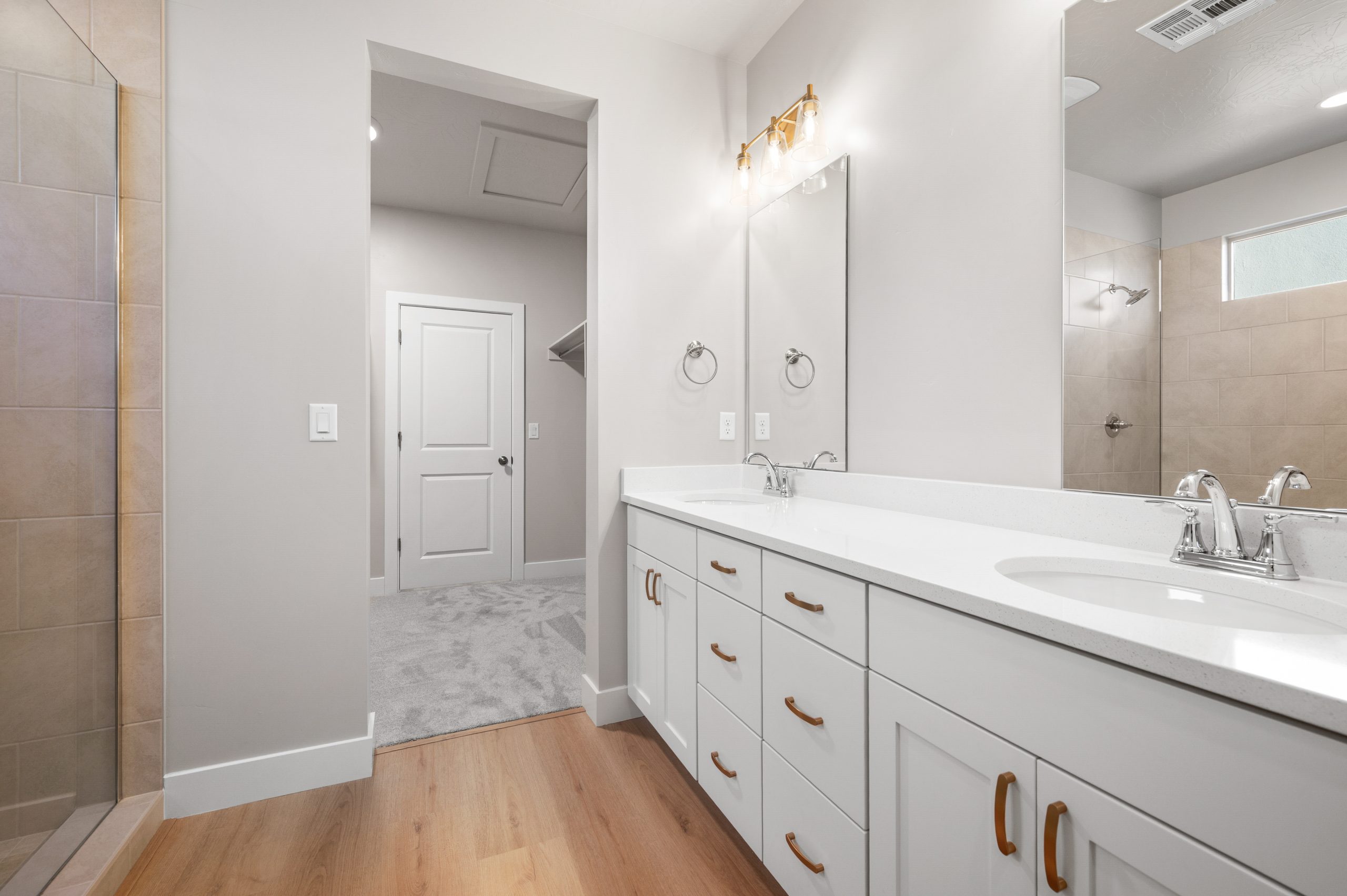 Spacious primary bathroom featuring a double-sink vanity, white cabinetry, gold hardware, and a tiled walk-in shower in the Mojave floor plan by Cole West.