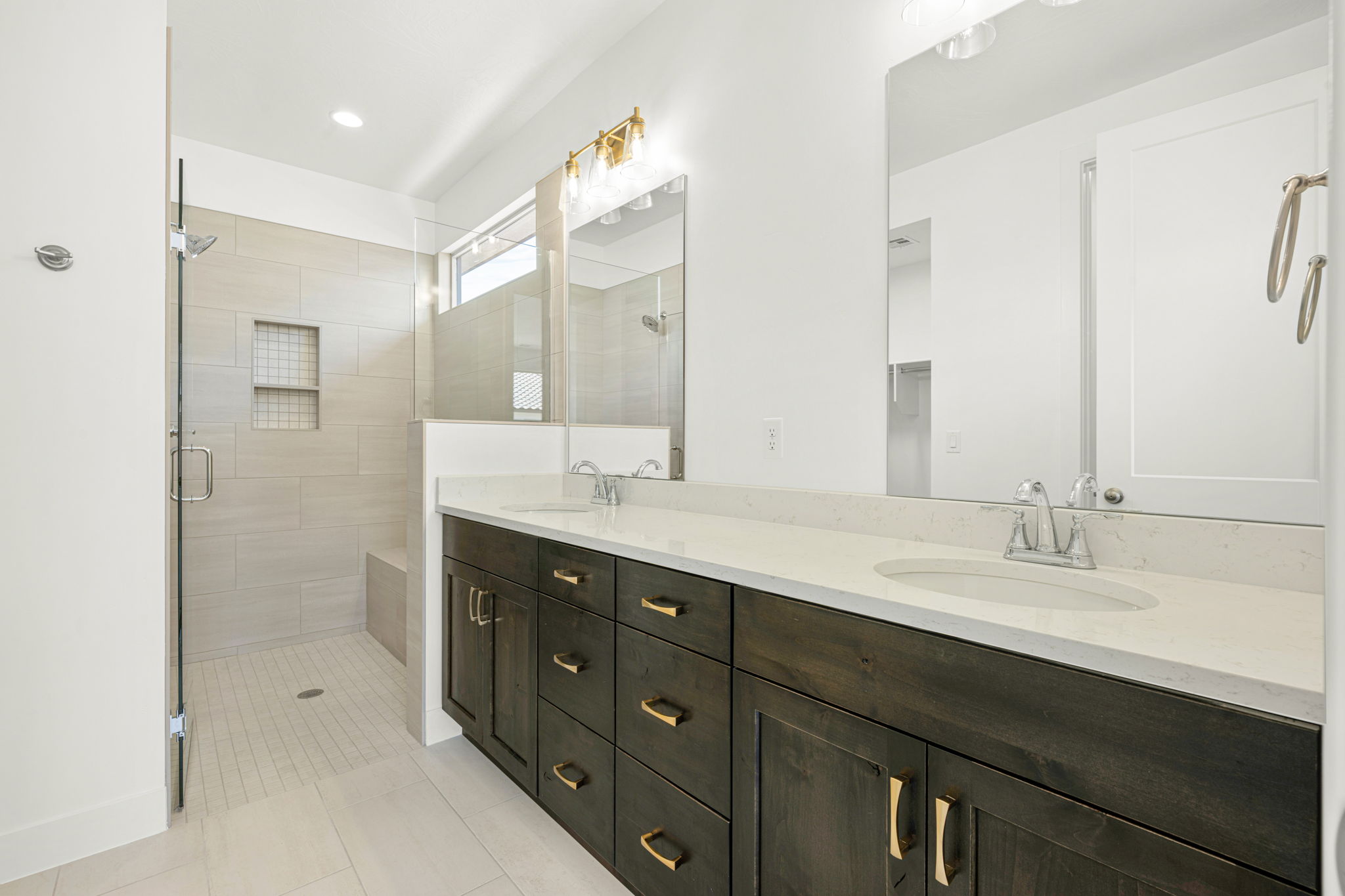 Primary bathroom in the Basin floor plan at Solis by Cole West, featuring a double-sink vanity, quartz countertops, dark wood cabinetry, and a spacious tiled walk-in shower.